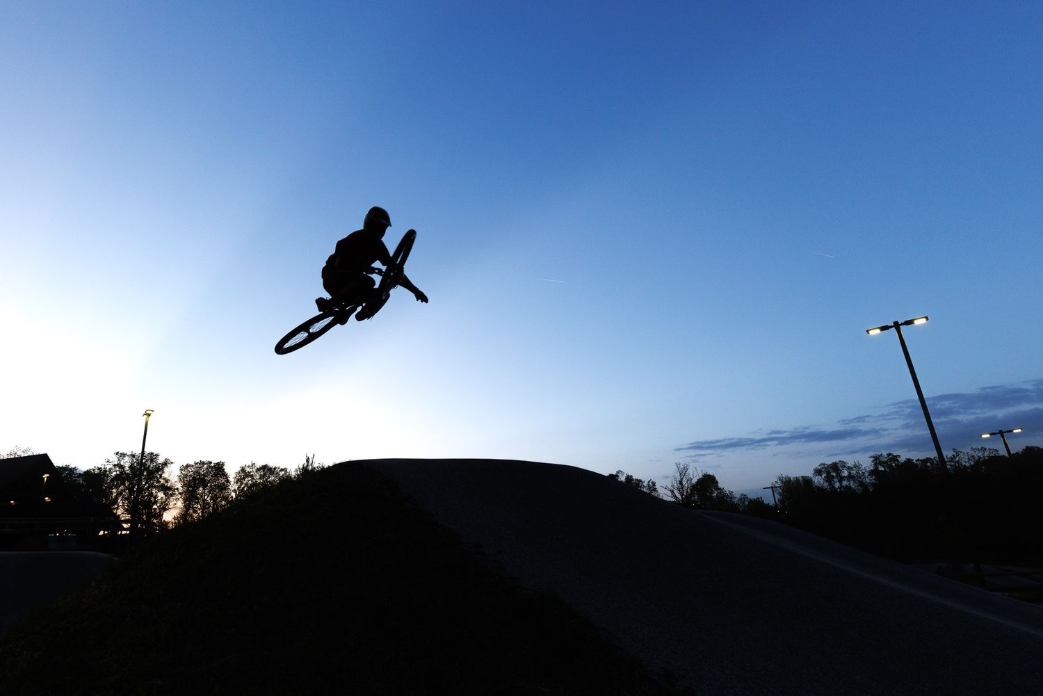 Dramatic silhouette of a BMX rider performing a high jump trick against a deep blue dusk sky.