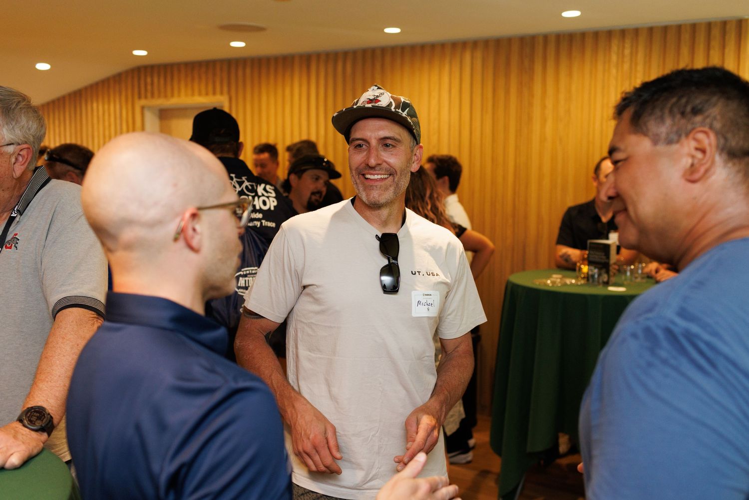 Three men laughing and socializing at an indoor cycling networking event.