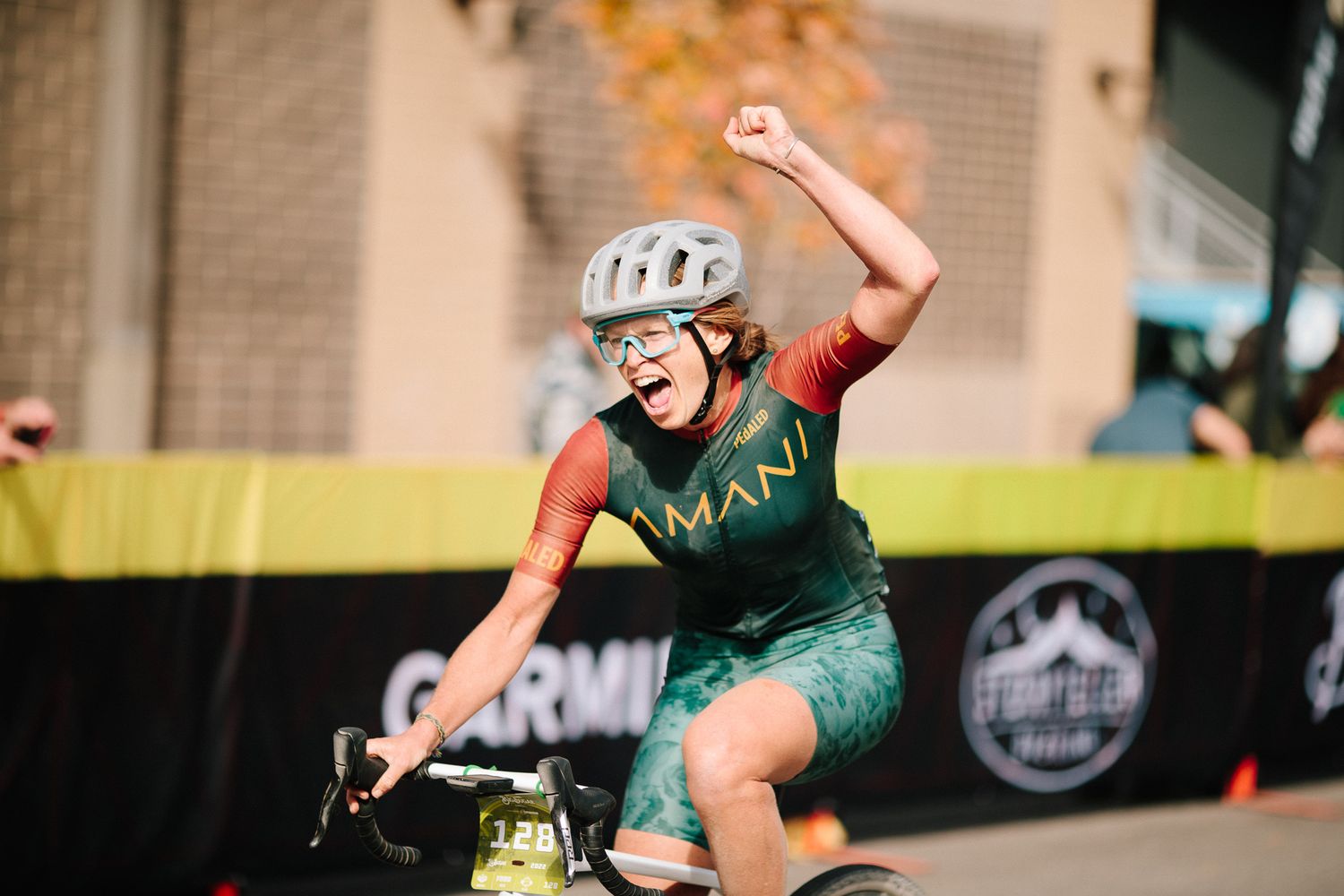 Excited female cyclist in Amani kit pumps her fist celebrating a victory at a cycling race finish.