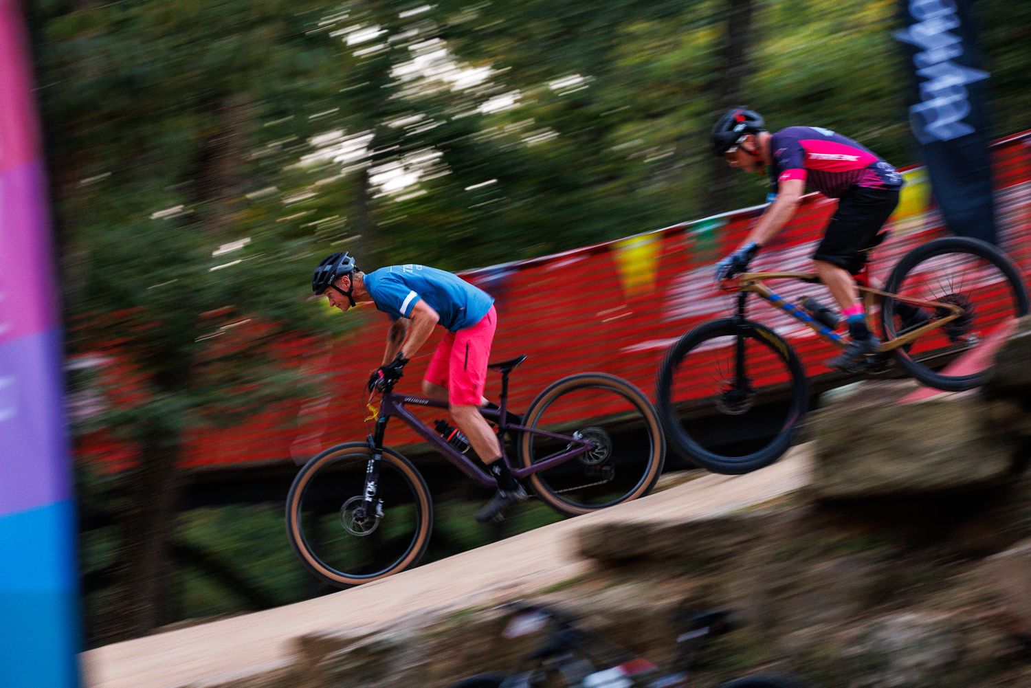 Two mountain bikers speed downhill in a blur during a competitive cycling race event.