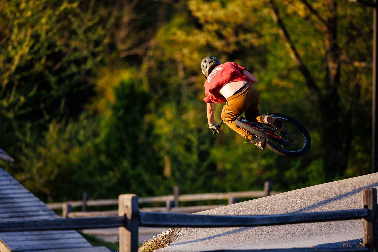 Mountain biker catching big air off a jump ramp at a bike park at sunset.