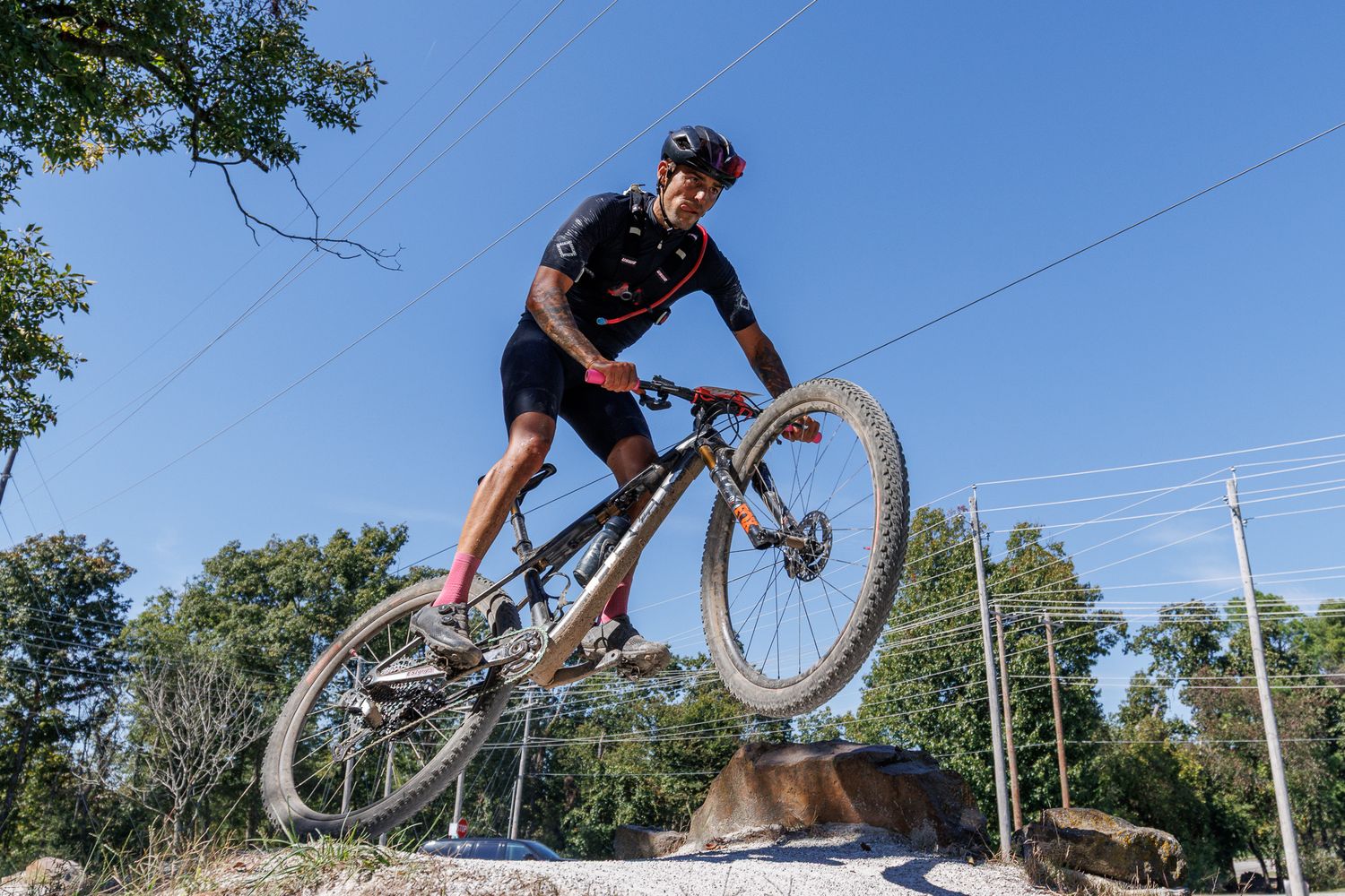 Mountain biker performing a jump on rocky terrain against a clear blue sky.