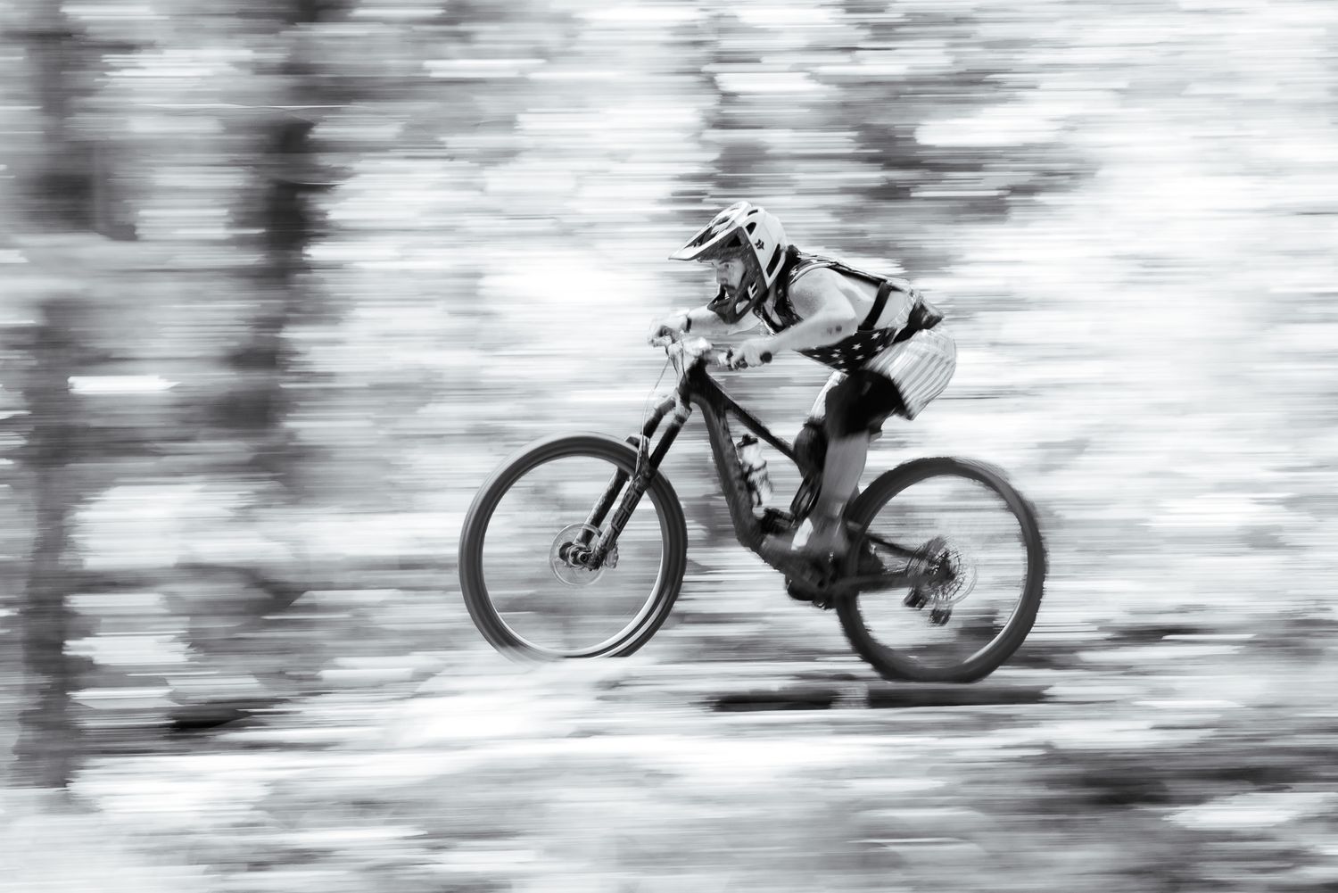 Black and white panning shot of a mountain biker speeding through a forest trail with motion blur.