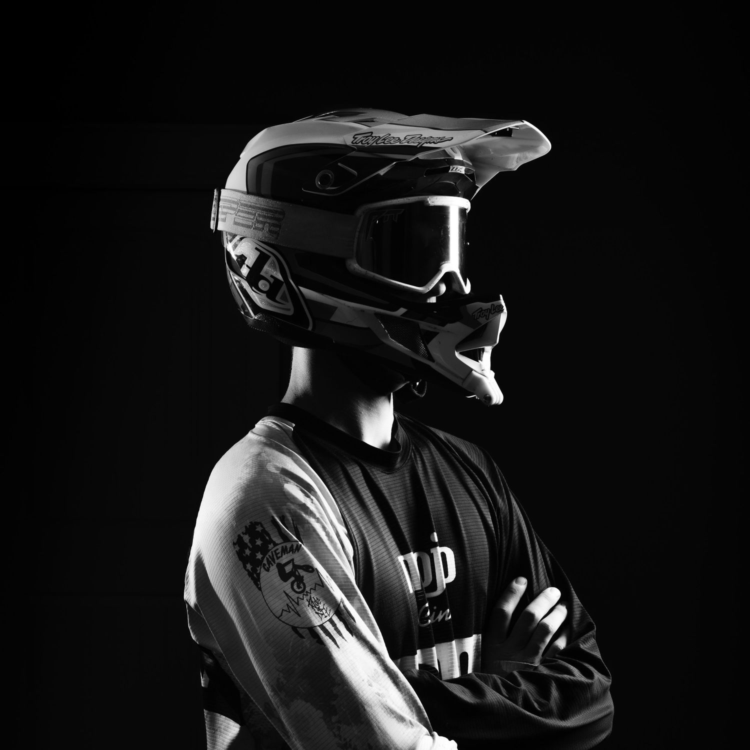 Black and white portrait of a motocross rider in helmet, goggles, and jersey with arms crossed.