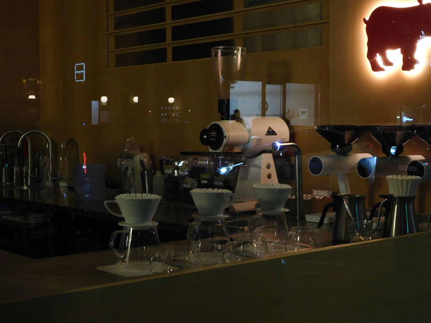 A dimly lit specialty coffee bar with espresso machines and pour-over equipment on the counter.