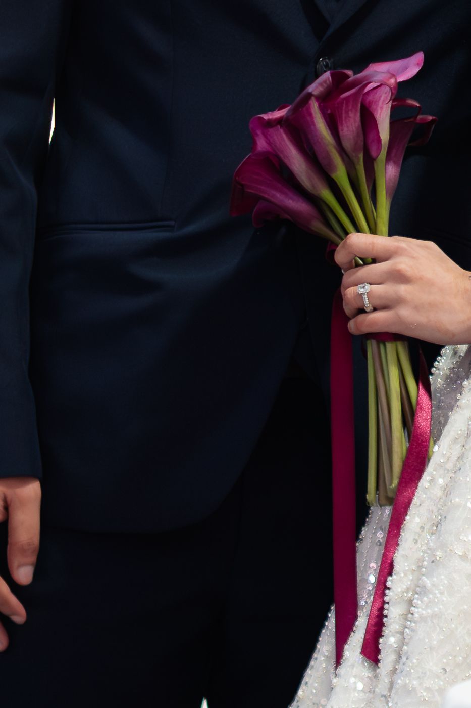 Bride in a white sequined gown holding a bouquet of deep purple calla lilies tied with burgundy ribbon.