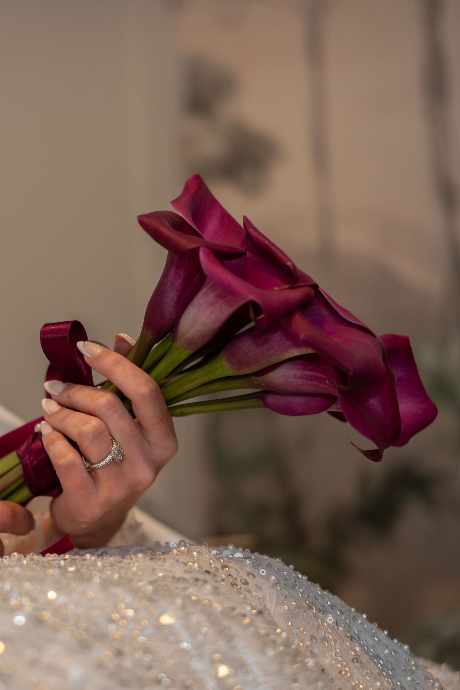 Bride holding an elegant bouquet of deep purple calla lilies with a burgundy ribbon against a white gown.