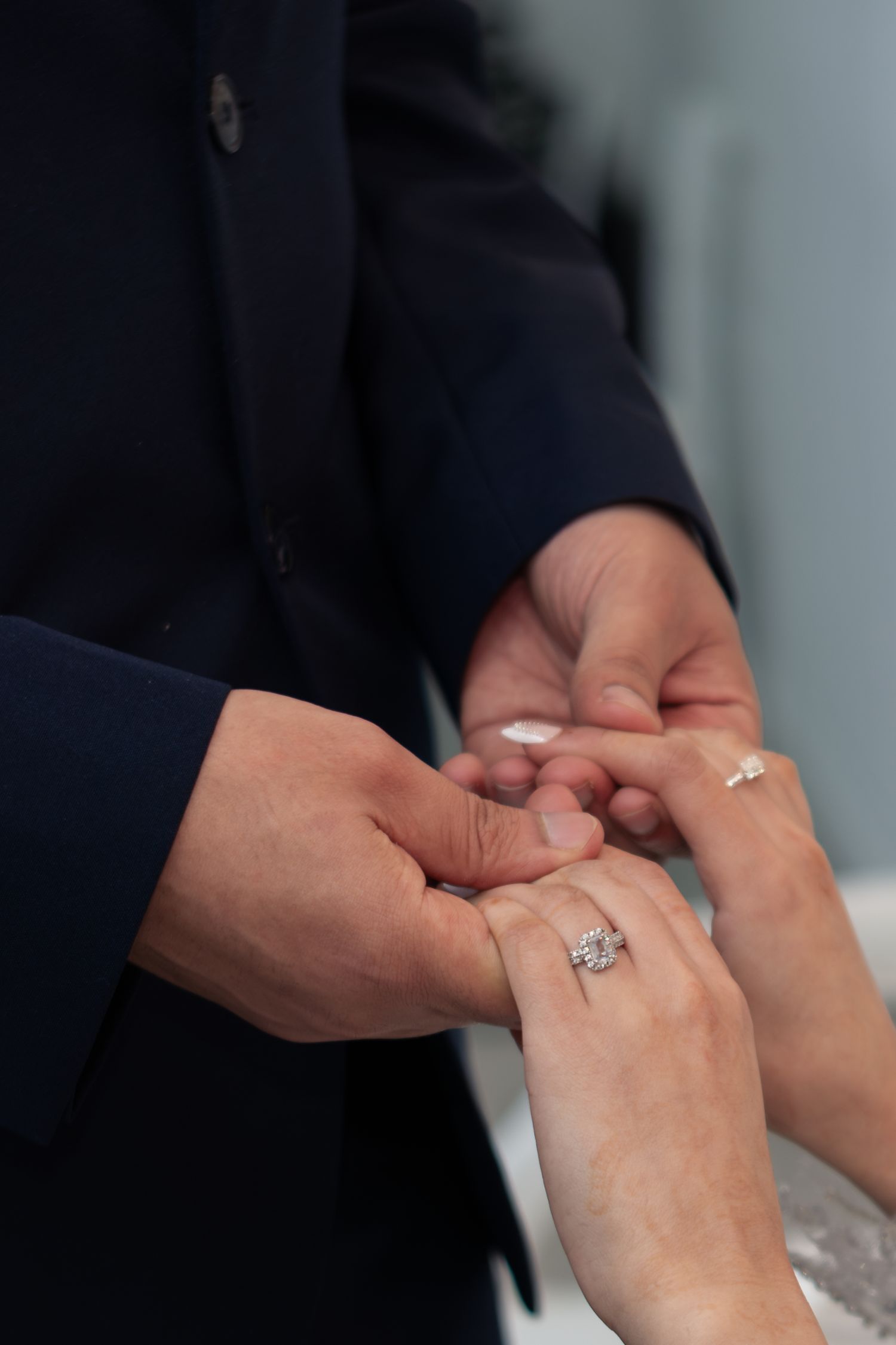 Close-up of a groom placing a diamond engagement ring on a bride's hand during a wedding ceremony.