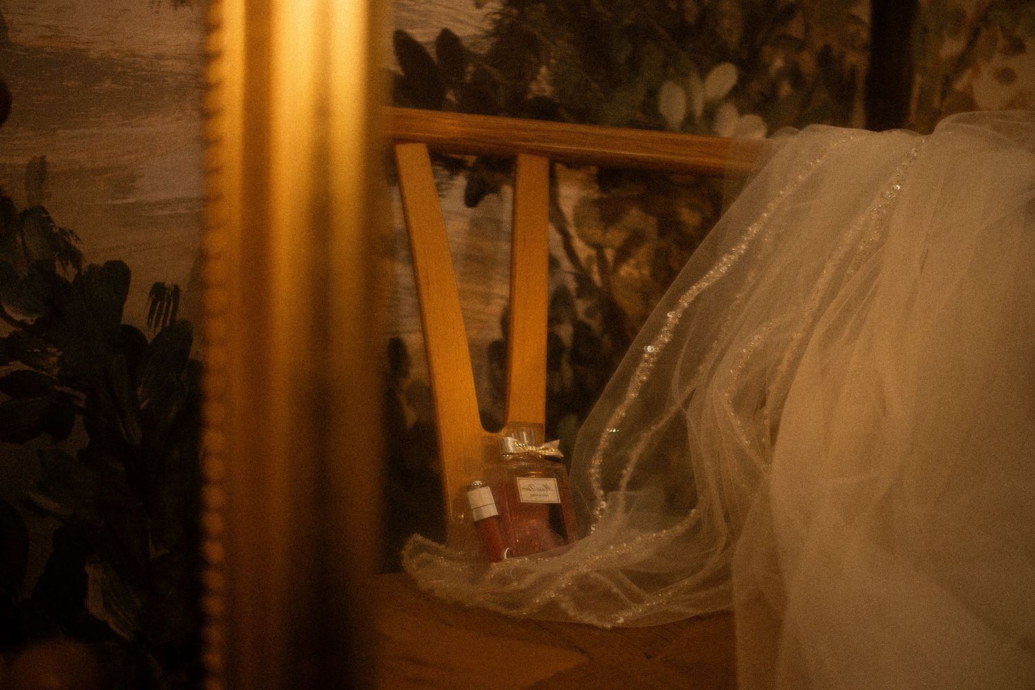 Elegant wedding veil draped over a chair beside a framed painting in warm golden light.