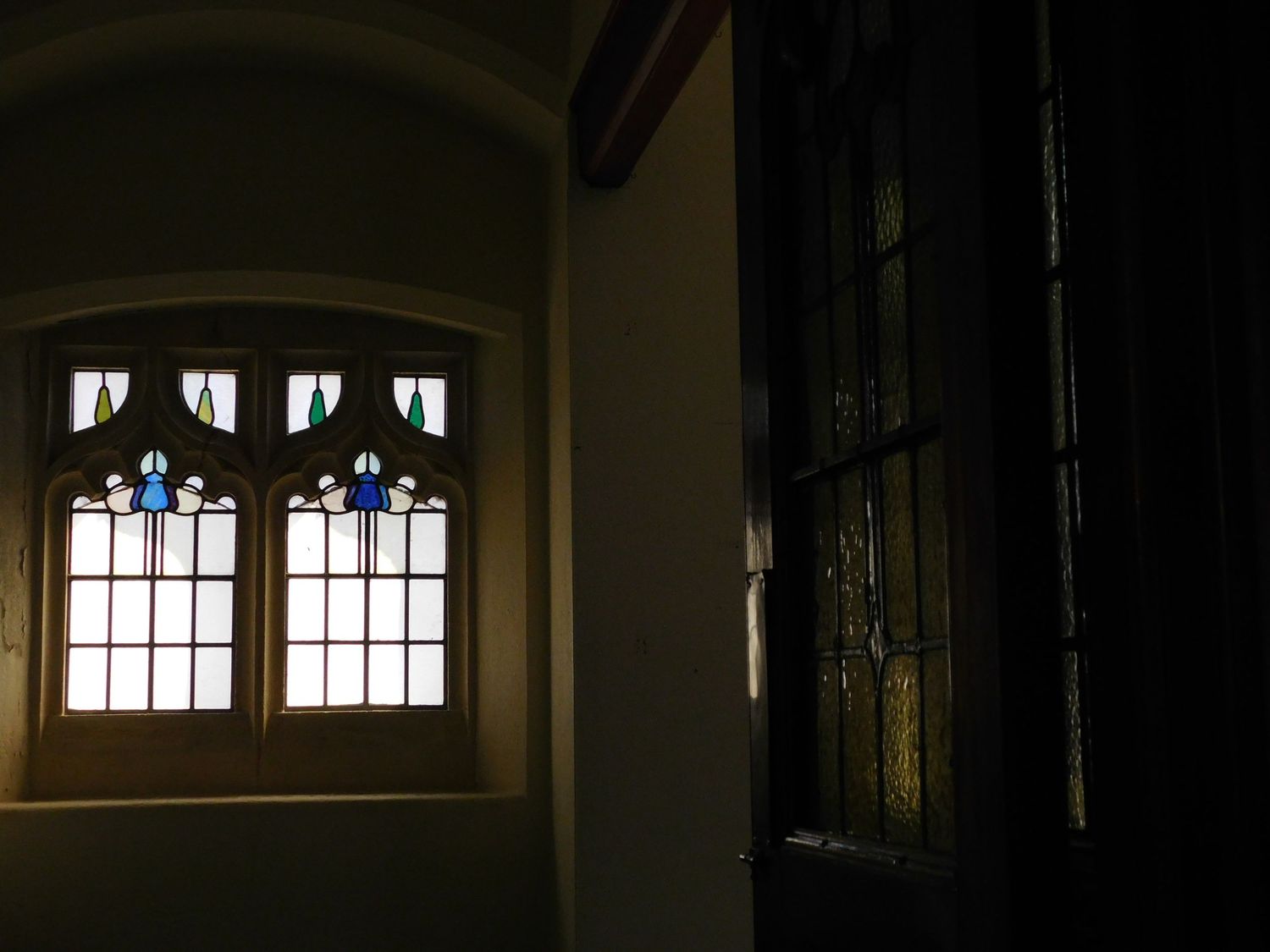 Ornate stained glass arched windows casting colorful light in a dark historic building interior.