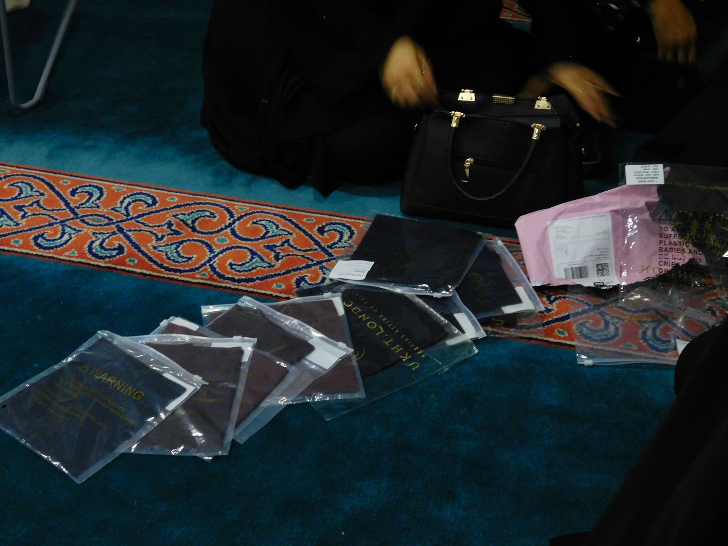 Black plastic-wrapped items and a handbag displayed on a colorful carpet.