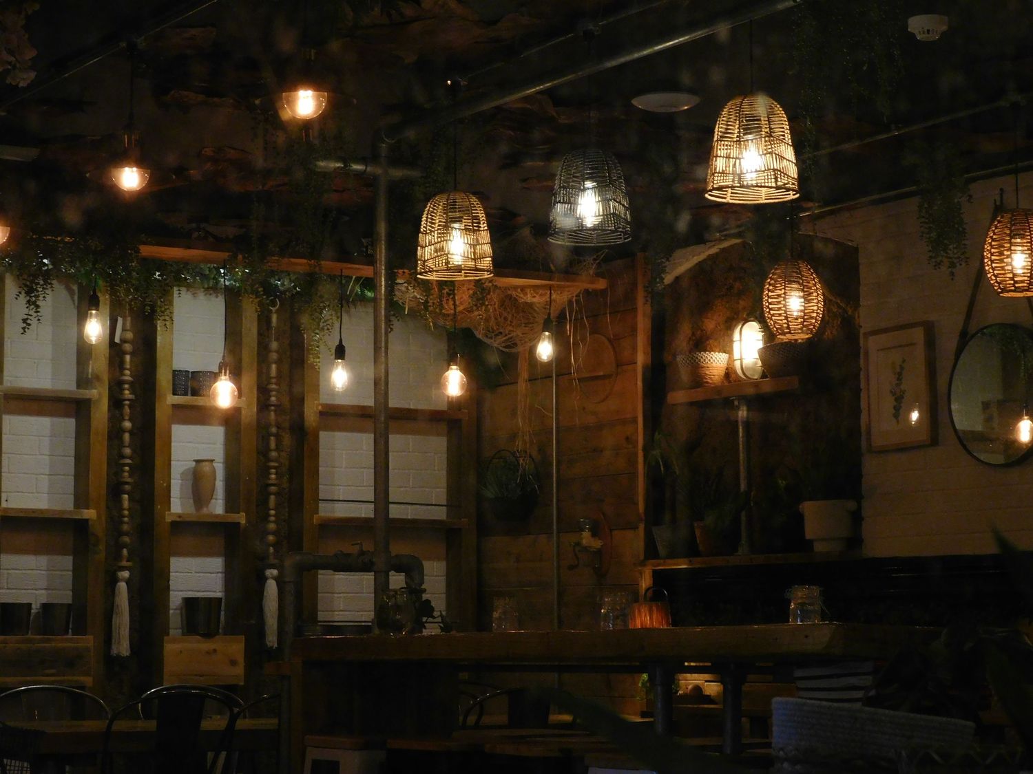 Cozy restaurant interior with warm Edison bulb pendant lights and wicker lampshades hanging from a dark ceiling.