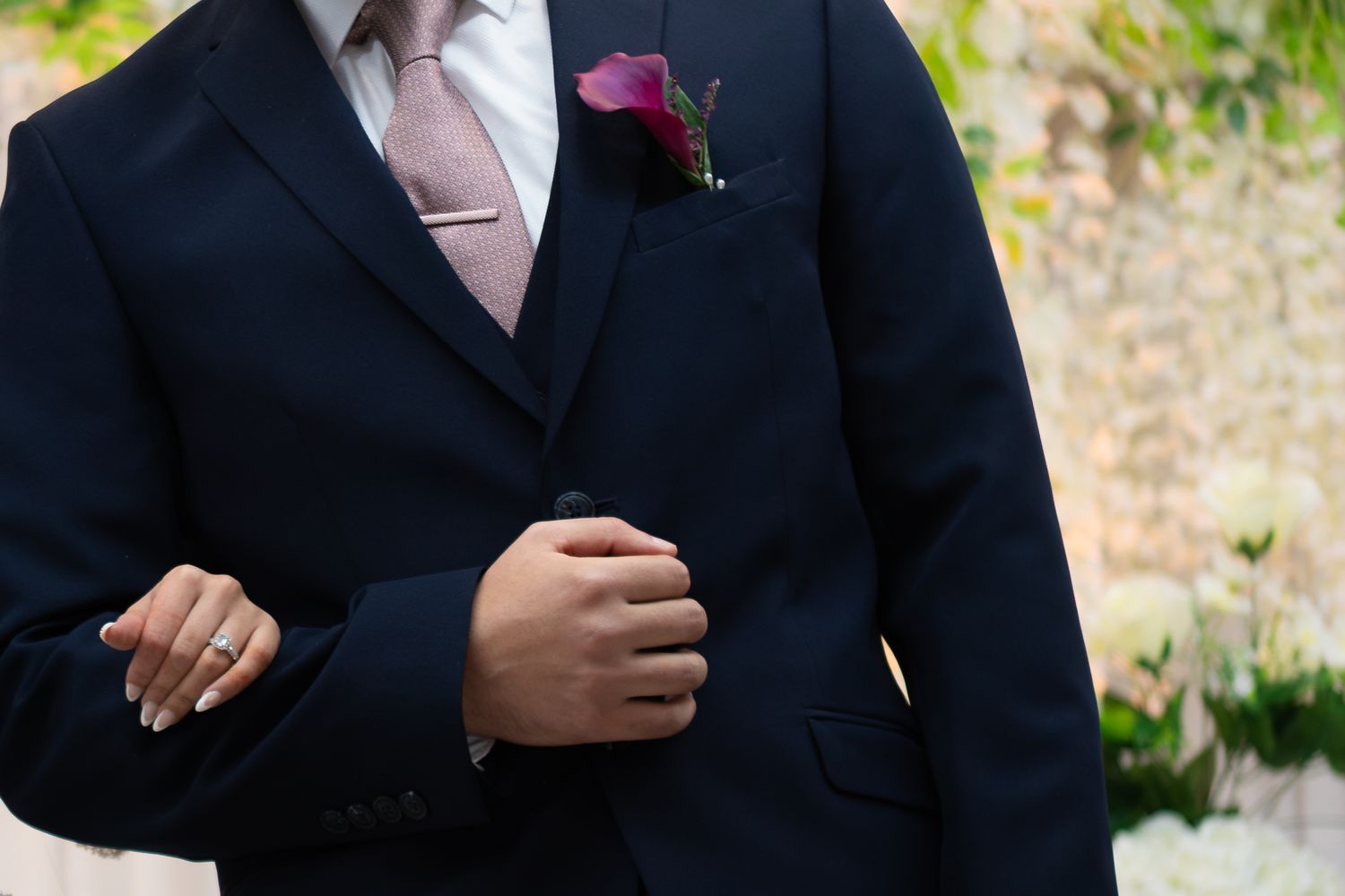 Groom in a navy three-piece suit with a pink tie and purple calla lily boutonniere at a wedding.