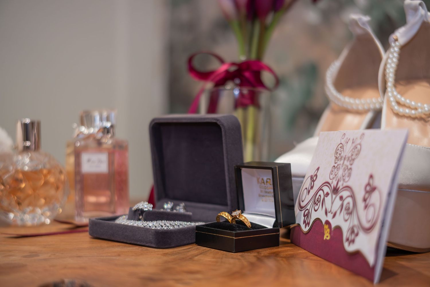 Wedding flat lay with jewelry boxes, gold rings, perfume bottles, pearl necklace, and floral gift bag.