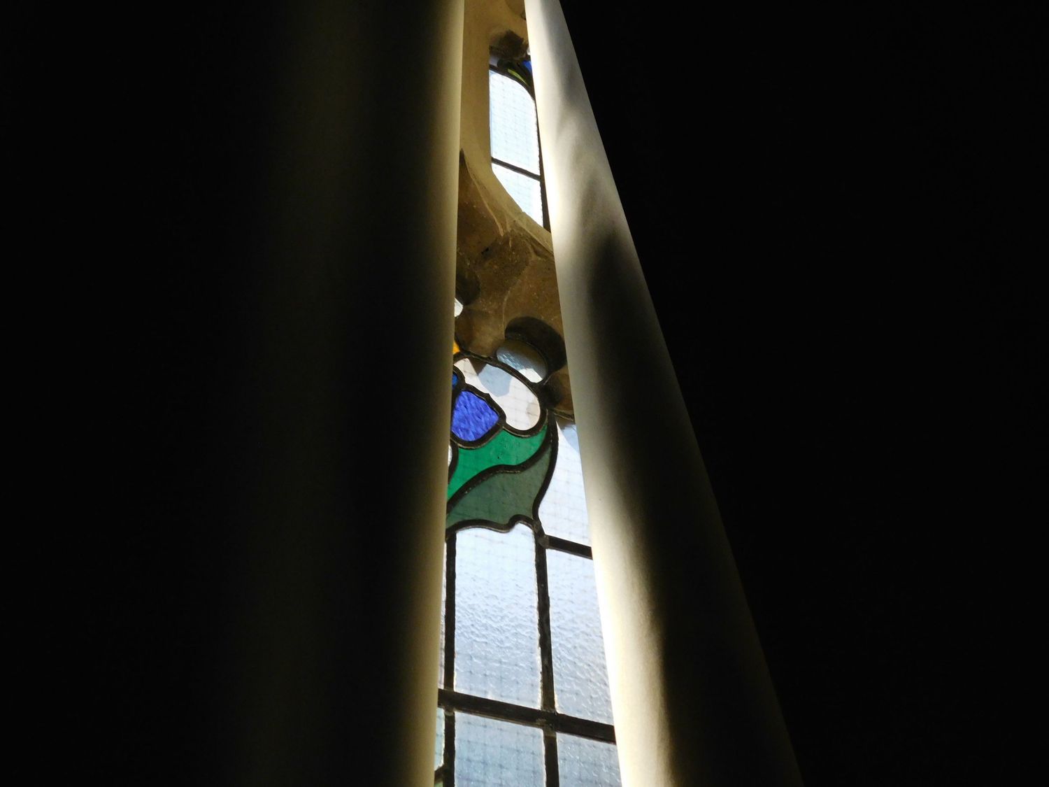 A narrow stained glass church window with blue and green decorative motifs seen through a gap.