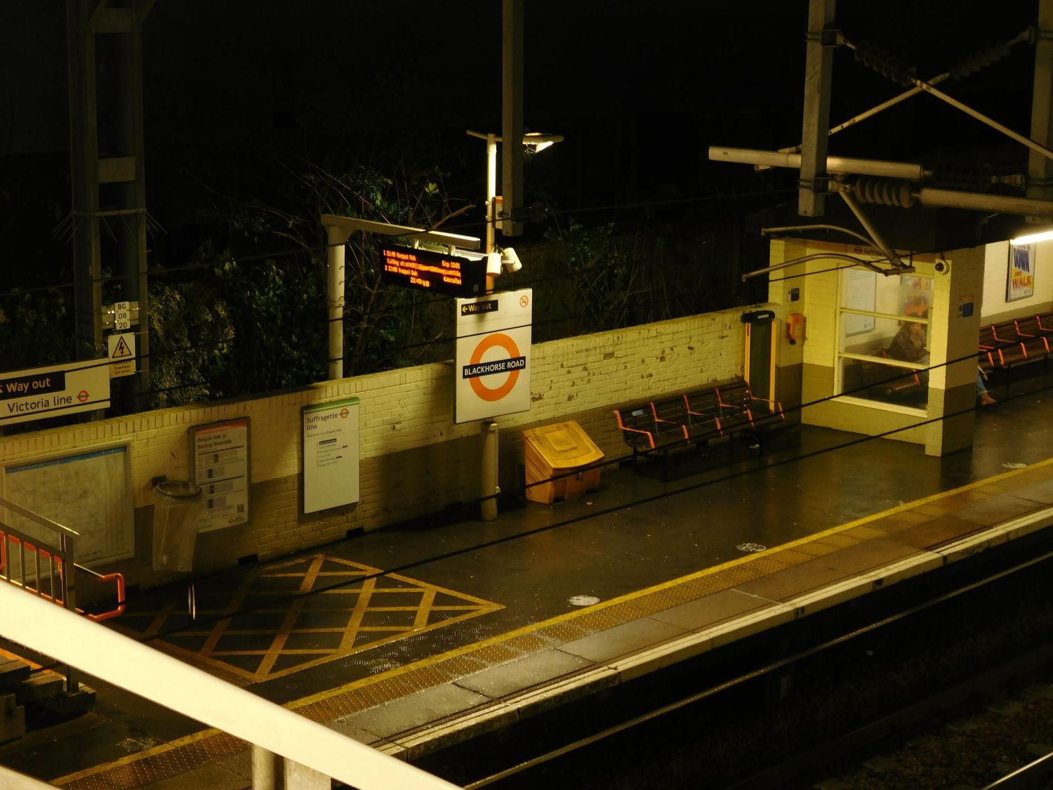 London Underground station platform at night with illuminated roundel sign and empty orange benches.