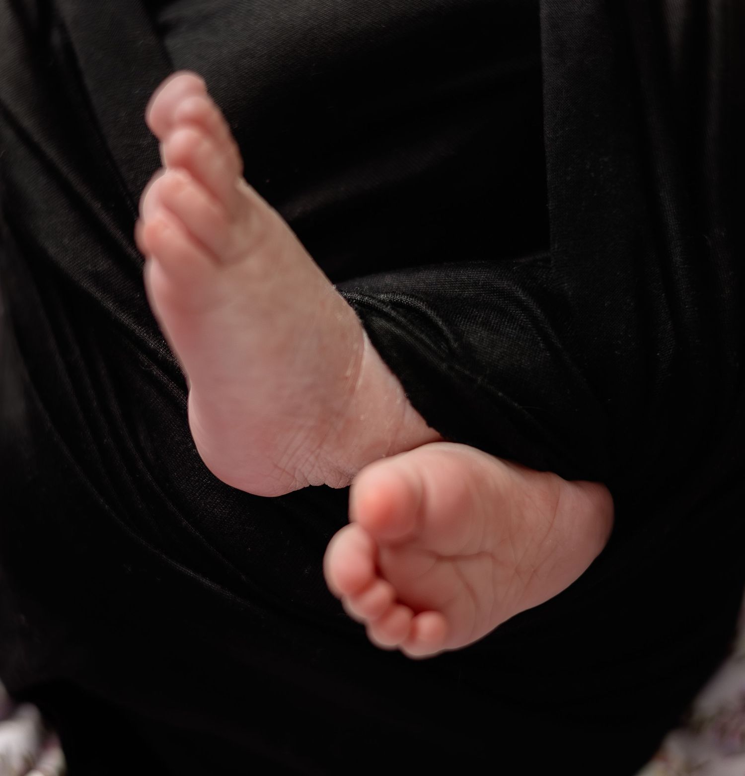 Close-up of a baby's tiny bare feet against a black fabric background.