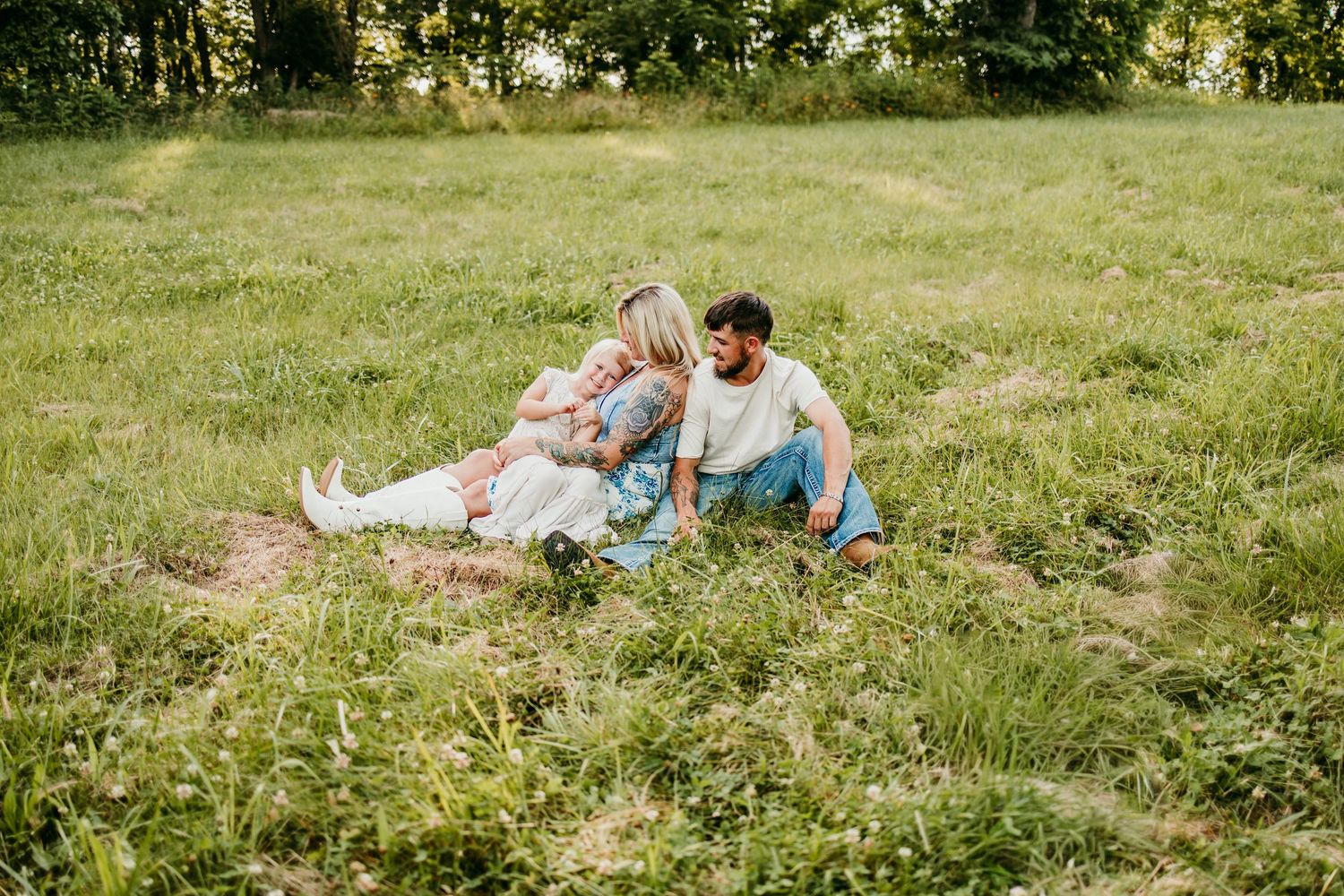 A couple sits together on a grassy field, sharing a tender moment outdoors on a sunny day.