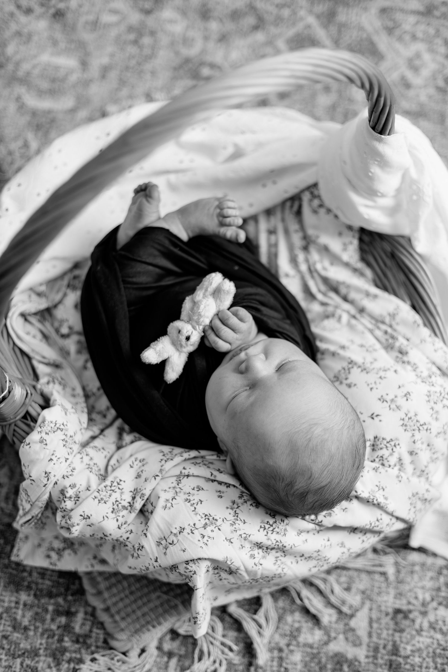 Black and white photo of a newborn baby lying in a basket, holding a small stuffed bunny toy.