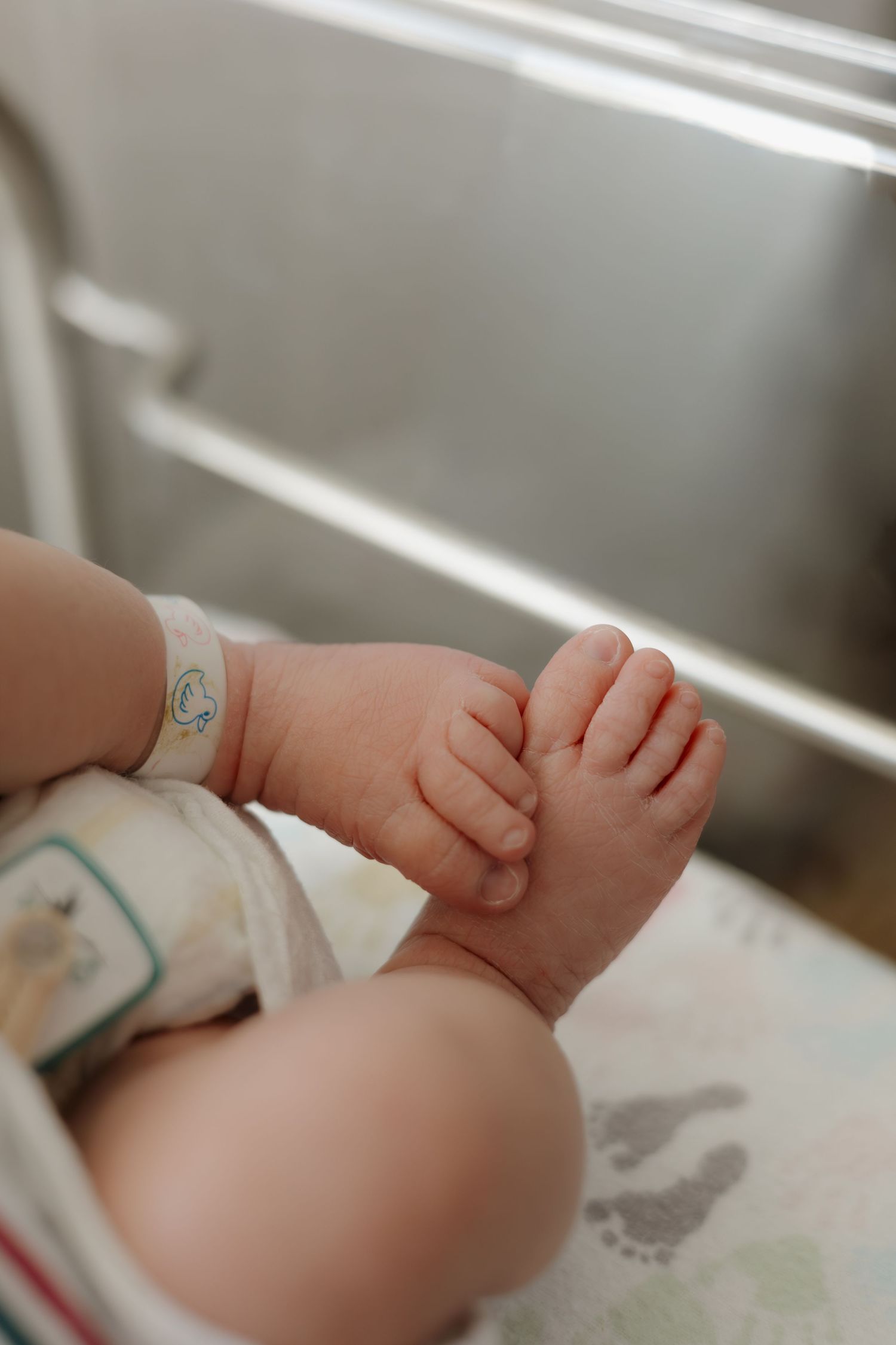 Close-up of tiny newborn baby feet with hospital identification bracelet, resting on a soft blanket in a nursery.