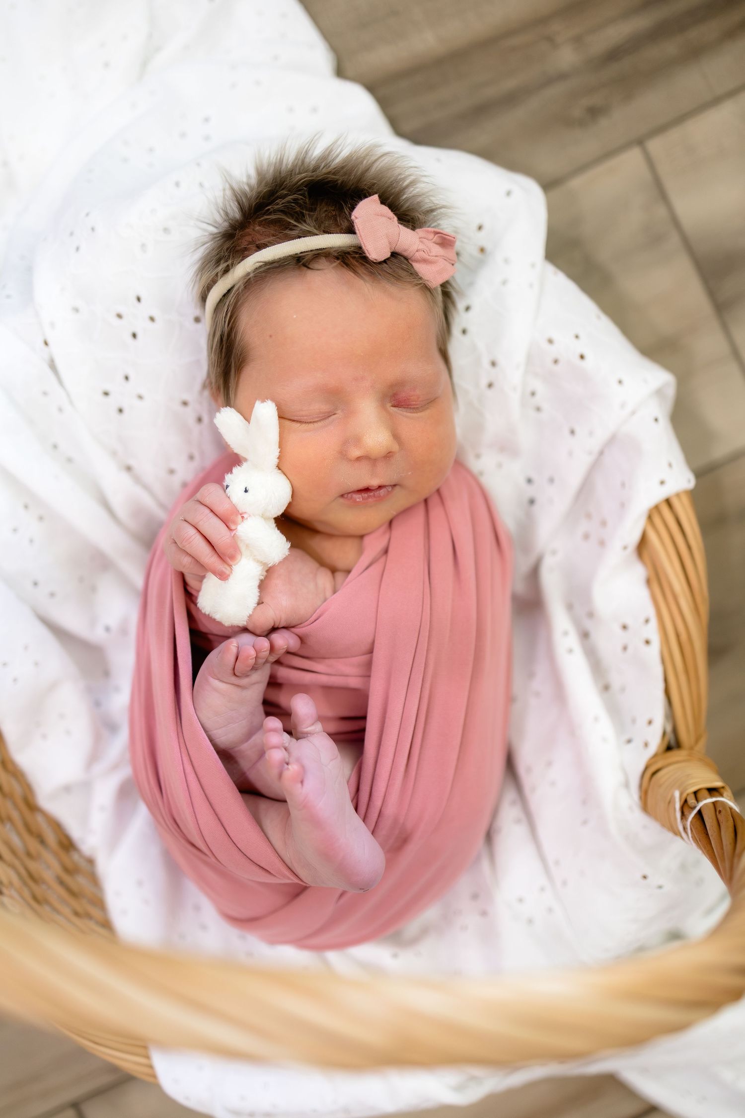 Sleeping newborn baby wrapped in pink swaddle holding a white bunny toy in a wicker basket.
