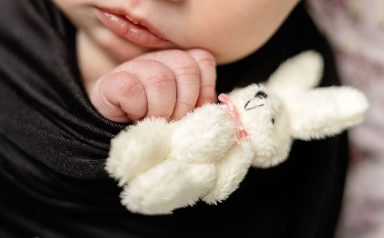Baby hand gently holding a small white plush bunny toy, close-up newborn photography.