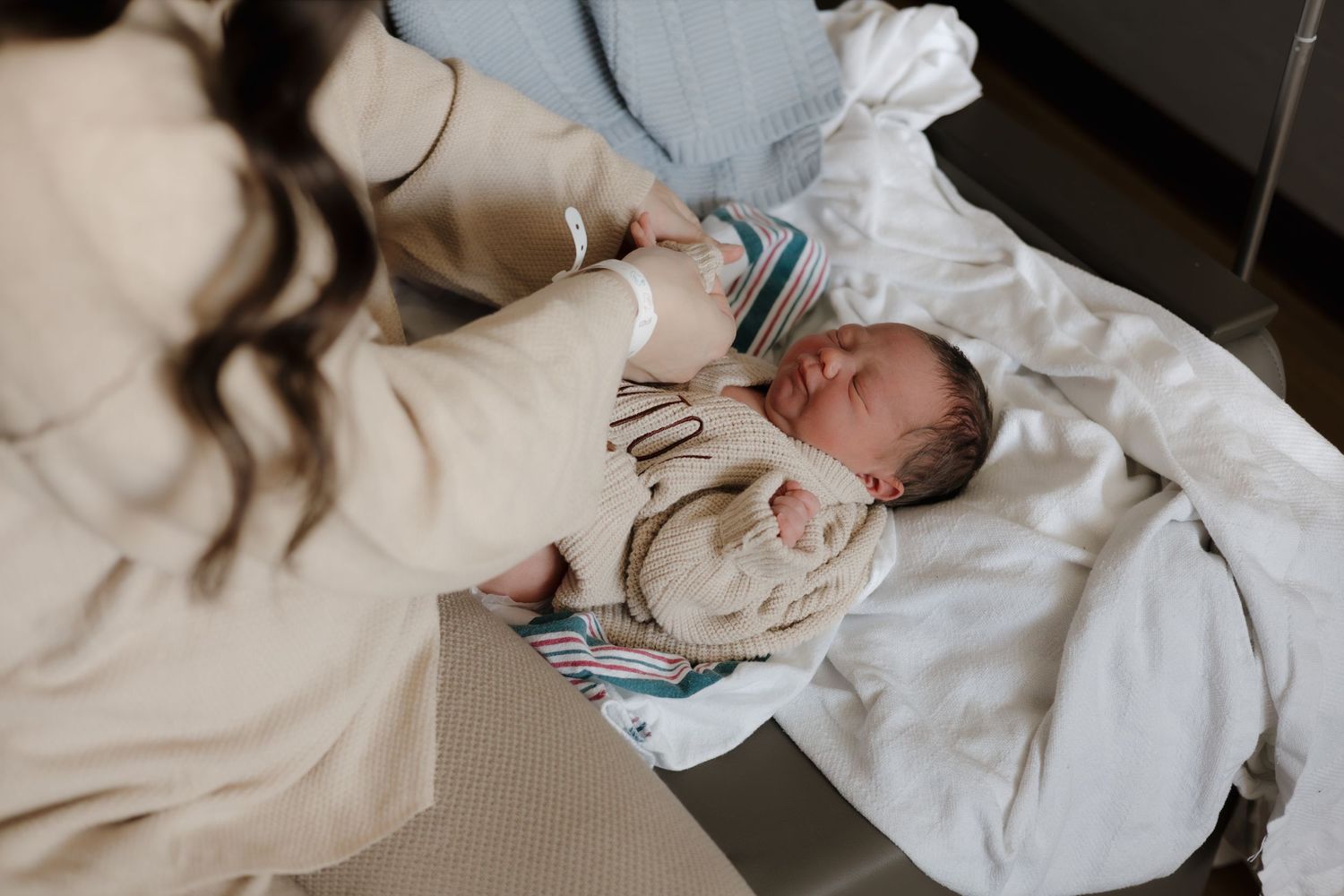 A mother tenderly holds her newborn baby on a hospital bed shortly after birth.