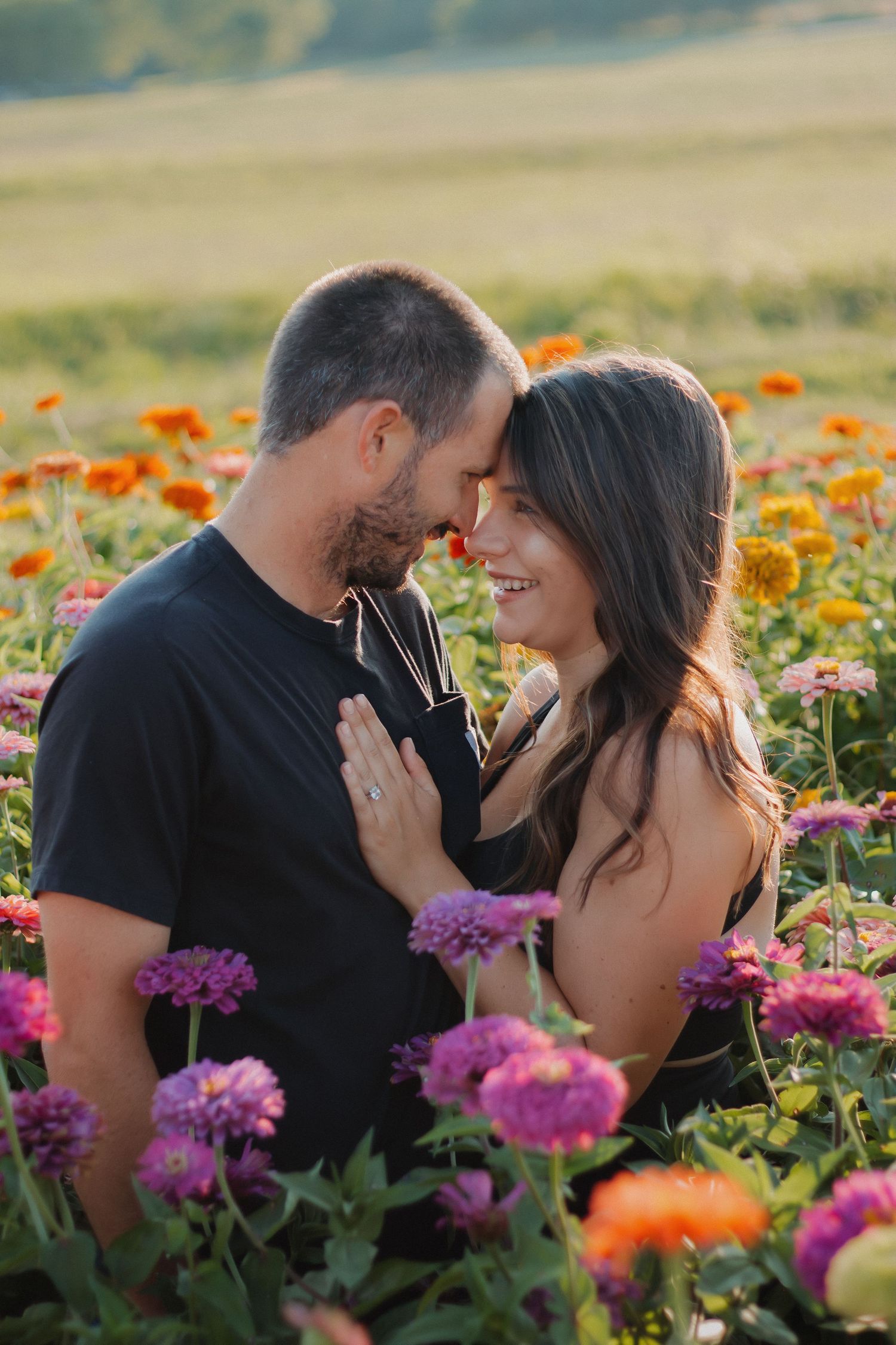 Couple sharing a romantic moment in a vibrant flower field with purple, orange, and pink blooms at golden hour.