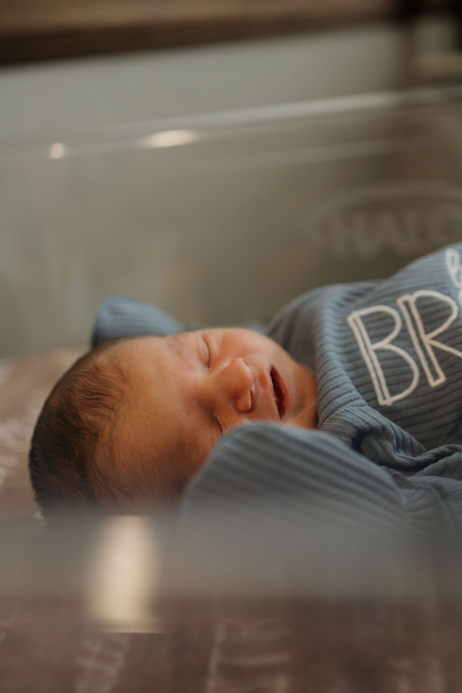 Newborn baby sleeping peacefully in hospital bassinet, swaddled in blue striped blanket with BR monogram.