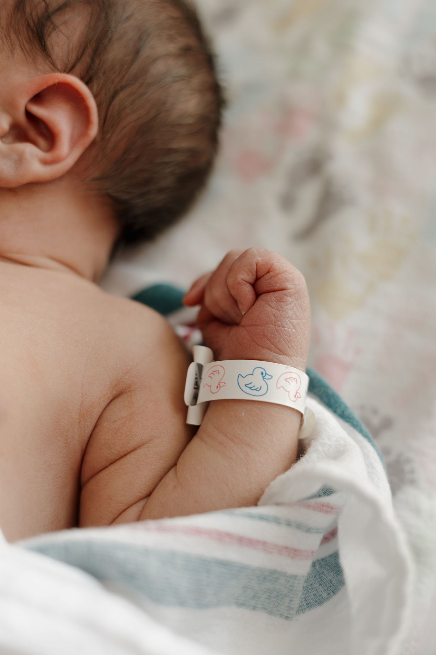 Newborn baby sleeping with a hospital identification bracelet on tiny wrist, wrapped in striped blanket.