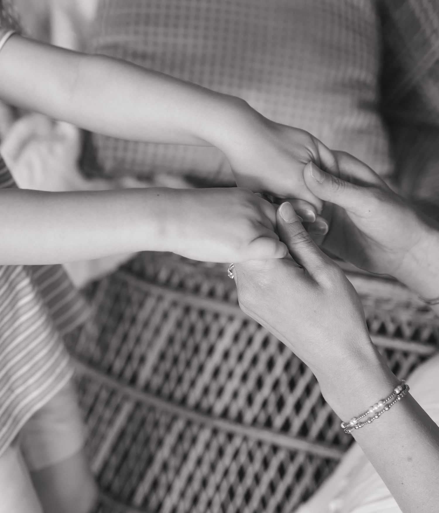 Black and white photo of two people holding hands tenderly, one wearing a beaded bracelet, symbolizing care and connection.