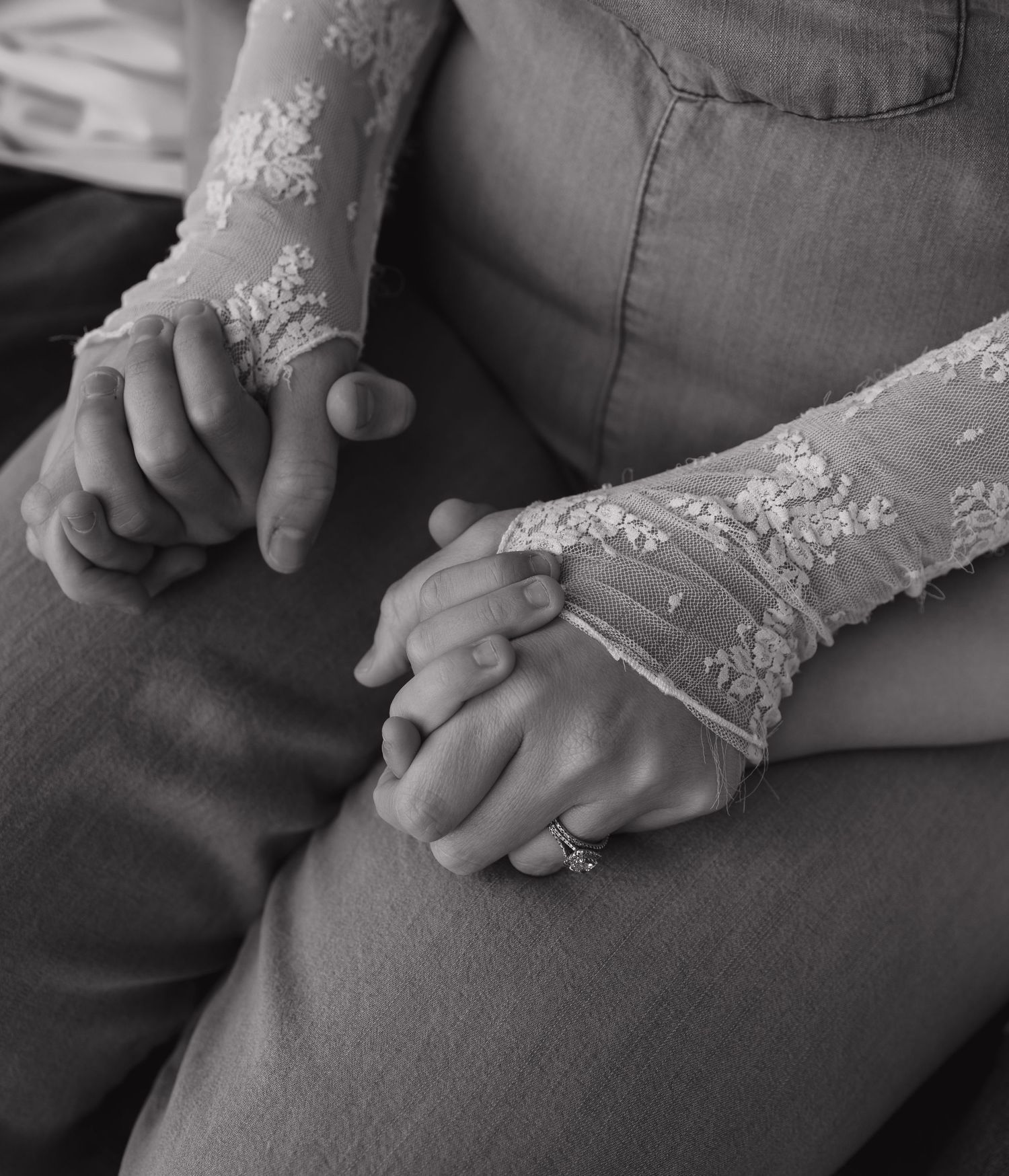Black and white photo of a bride and groom holding hands, showcasing lace wedding dress sleeve and a ring.