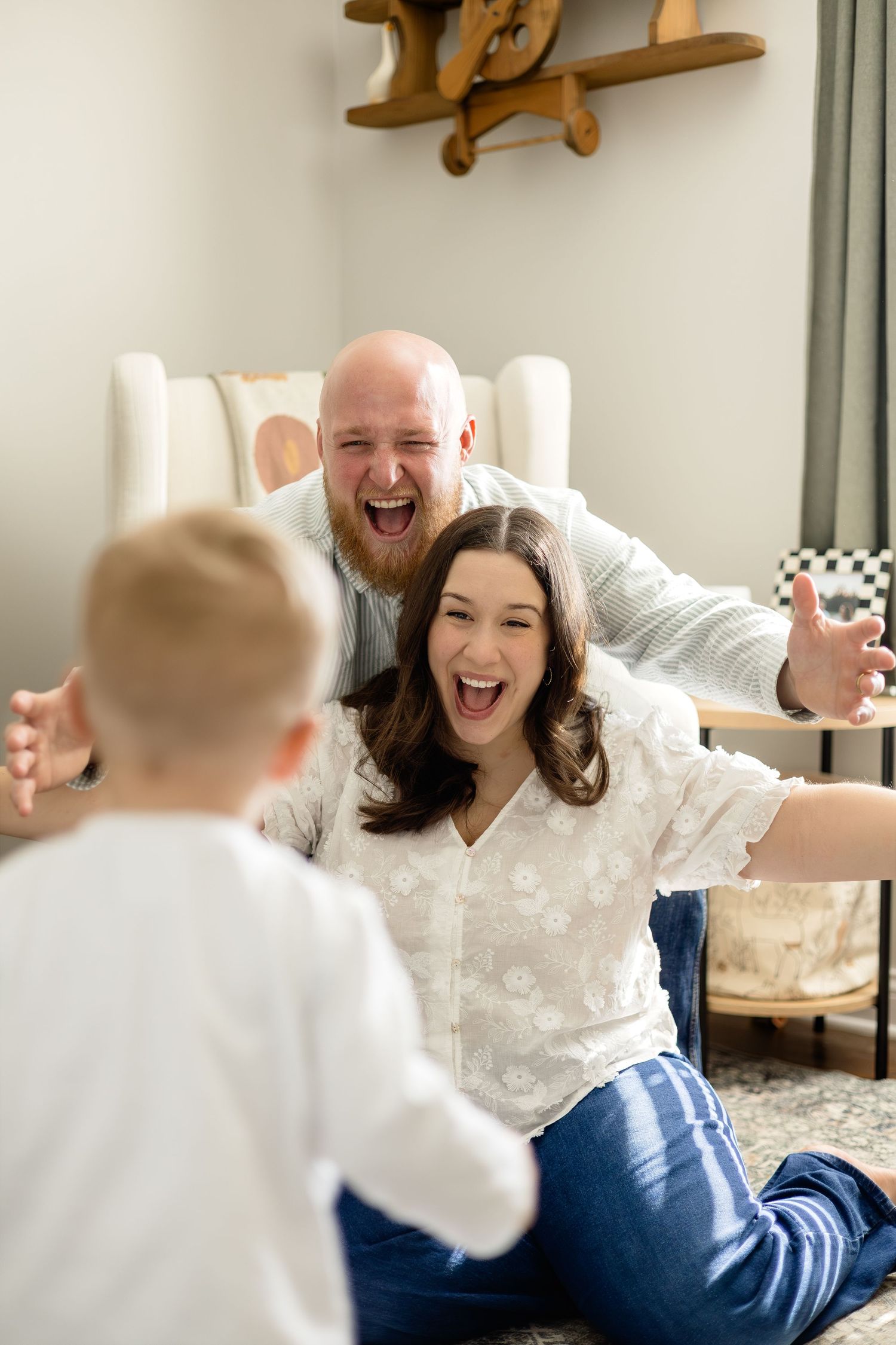 Excited parents with open arms welcoming their toddler in a bright nursery room.