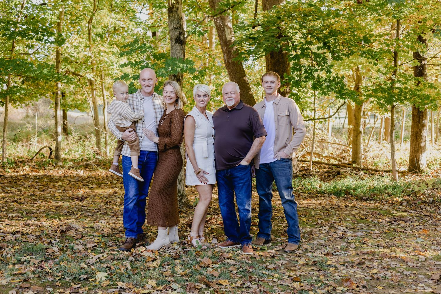 Family of six posing outdoors in autumn forest with colorful fall foliage during a professional family portrait session.