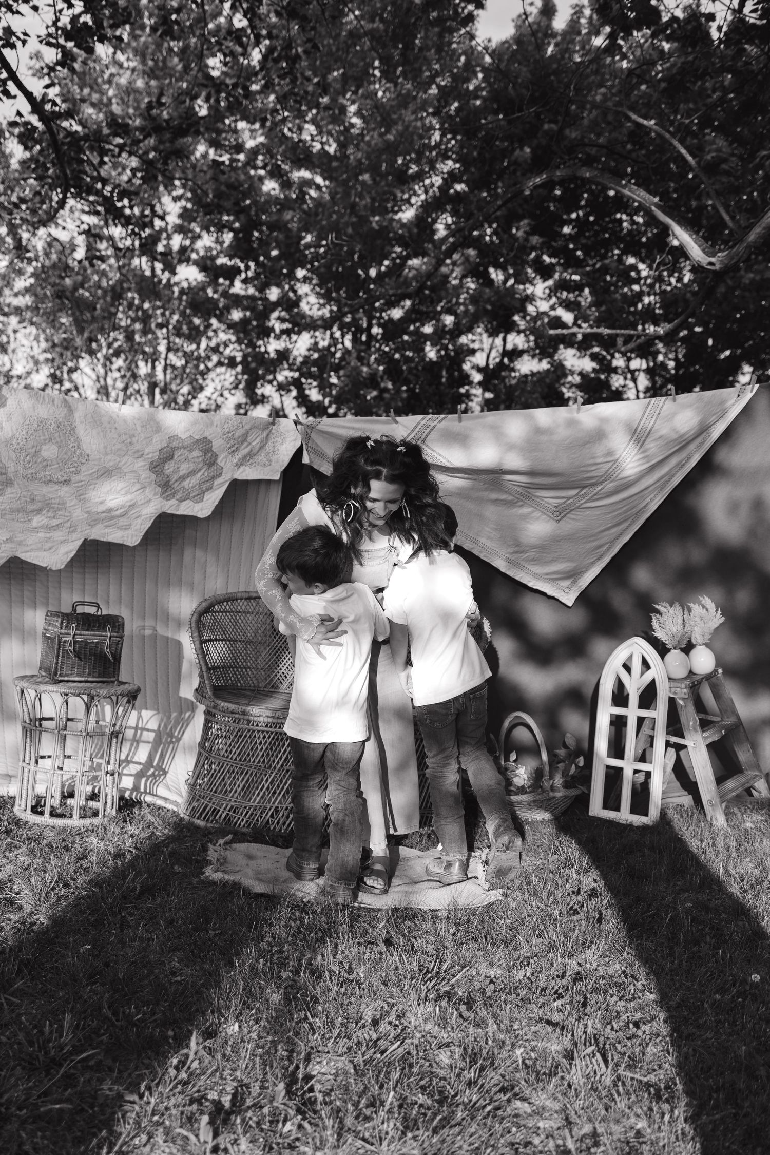 Black and white photo of children playing under a fabric canopy in a backyard with vintage furniture and trees.