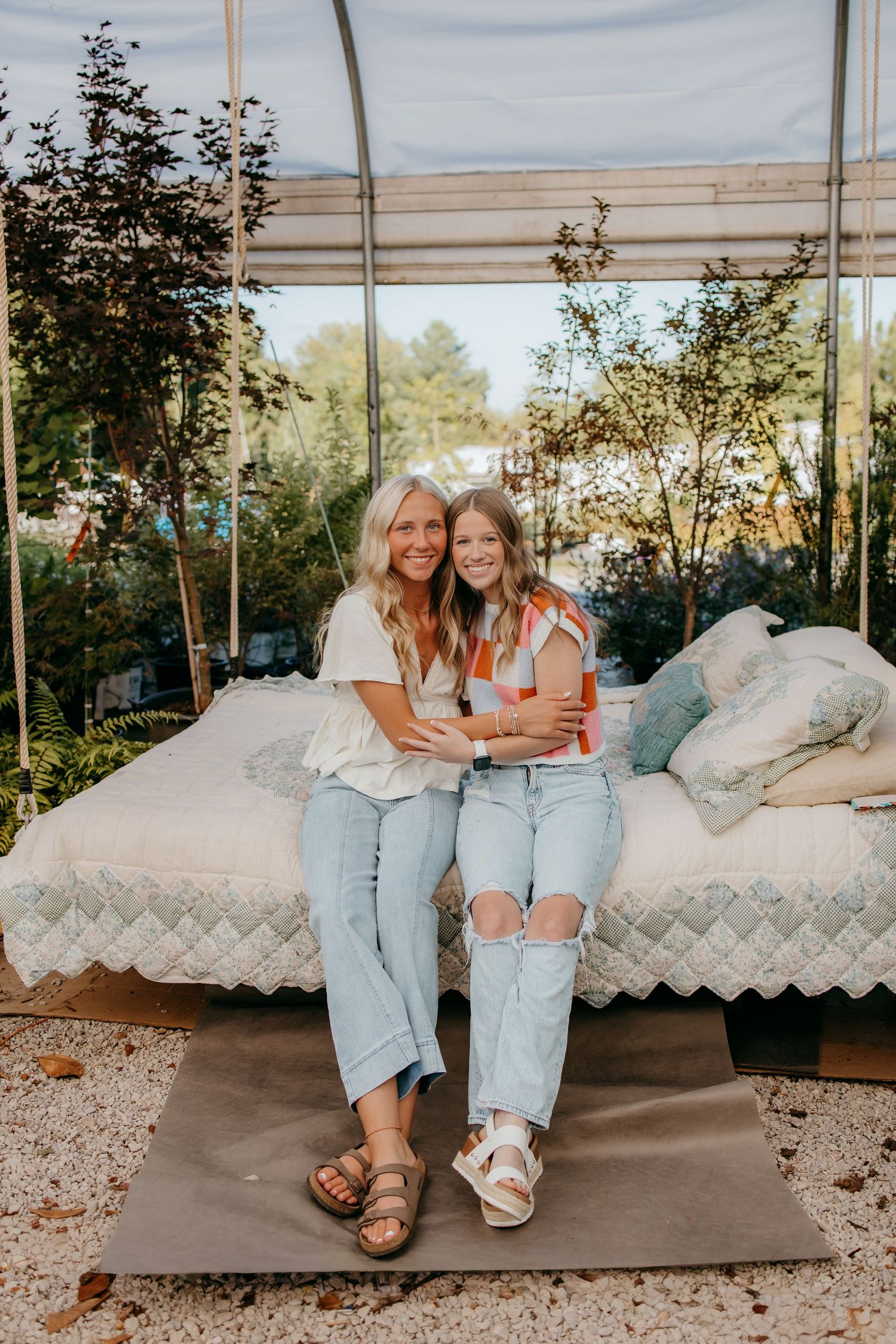 Two seniors smiling and sitting together on an outdoor swing bed surrounded by lush greenery.