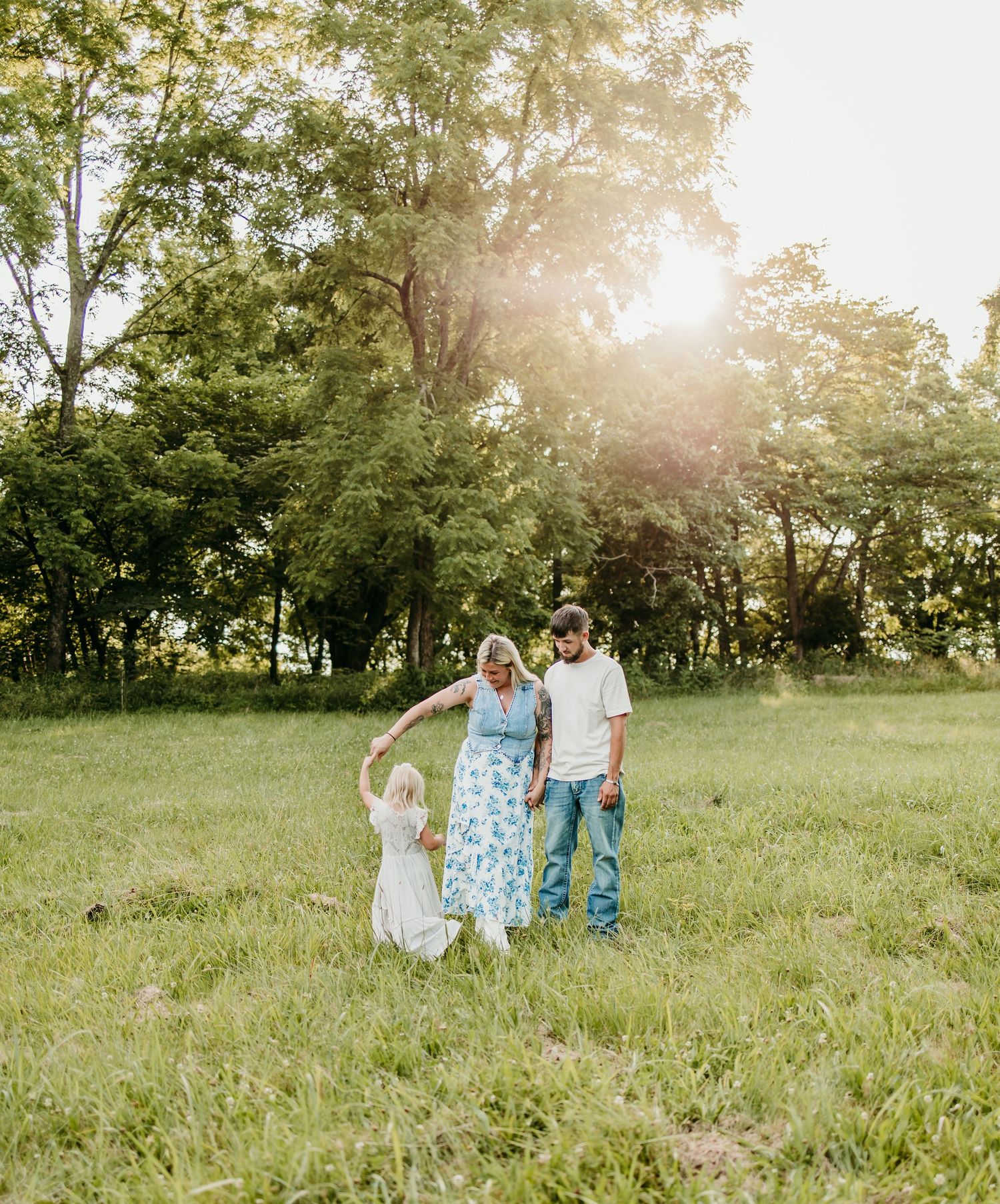 Family of three enjoying a sunny day in a lush green meadow, with parents dancing with their young child.