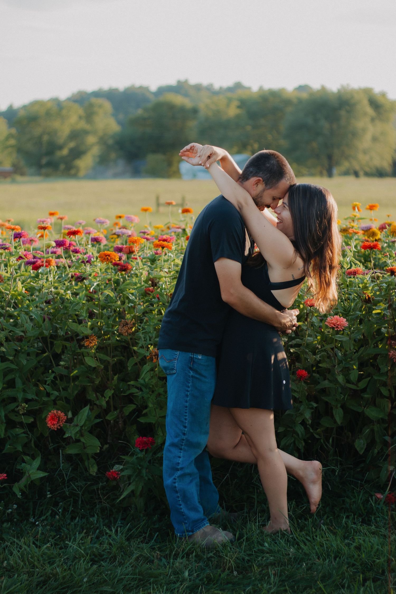 Couple dancing and kissing in a colorful zinnia flower field during golden hour outdoors.