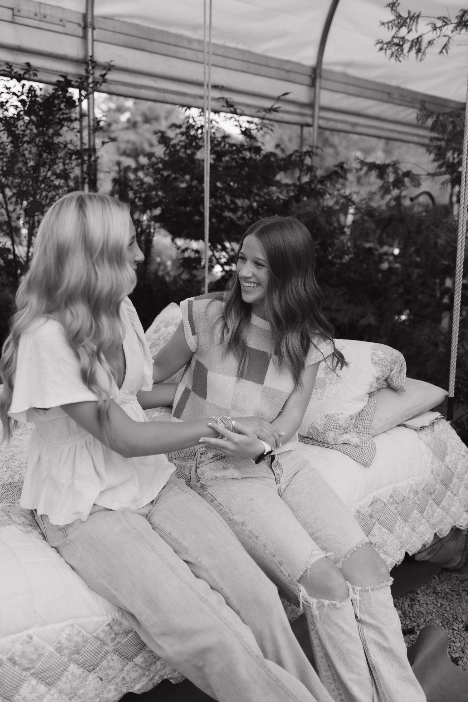 Two seniors sitting on a swing bed outdoors, smiling and holding hands in a black and white photo.