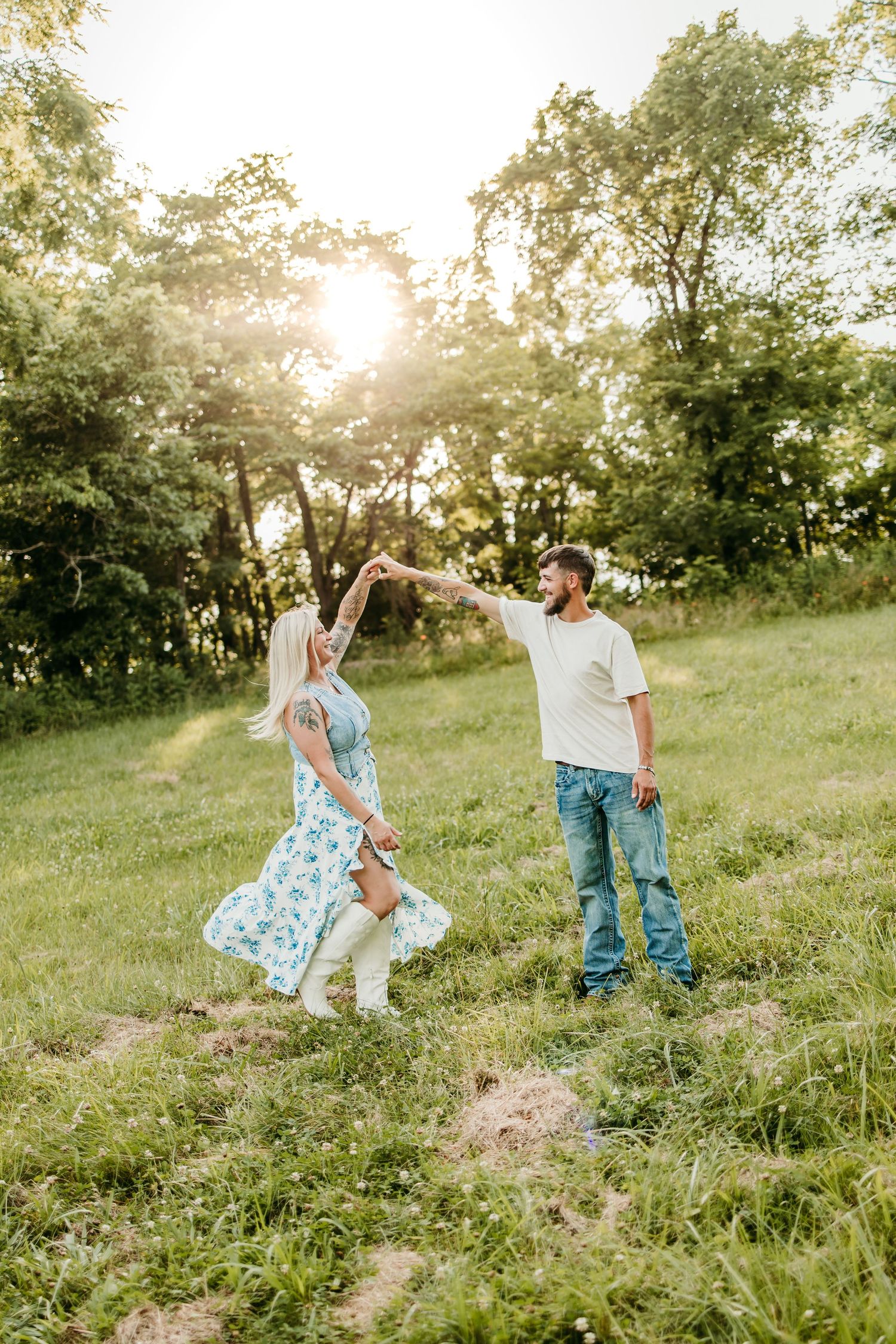 Couple dancing outdoors in sunlit green field, woman in floral dress spinning, man in jeans and white tee, golden hour.