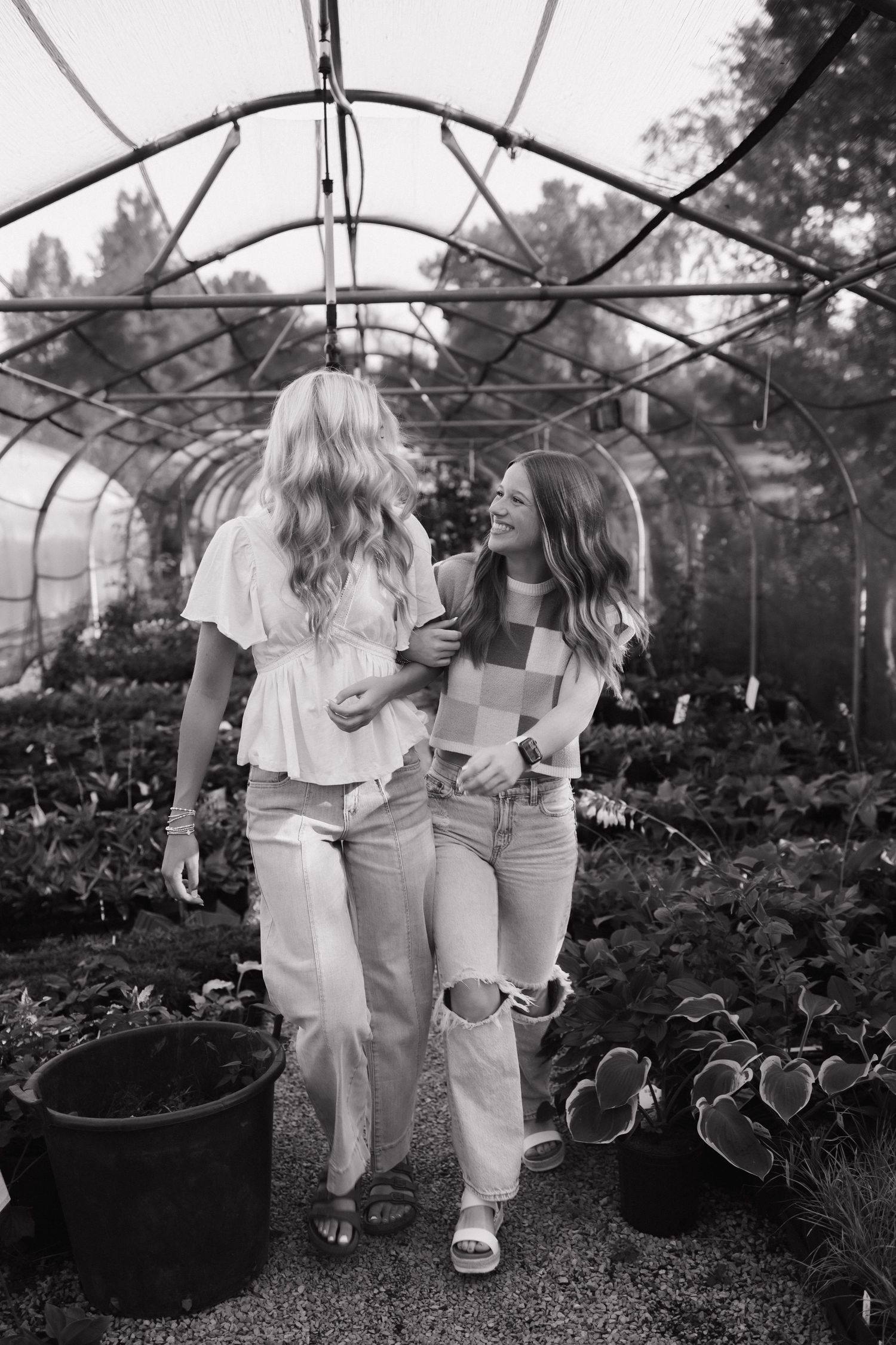 Two seniors smiling and walking together through a greenhouse filled with plants, black and white photo.