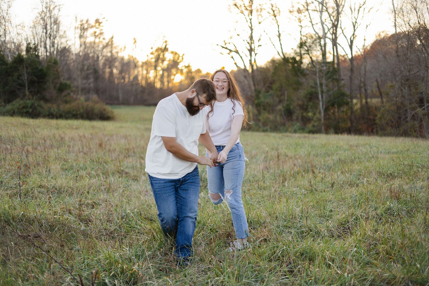 Couple laughing and walking together in a golden sunset field surrounded by autumn trees.