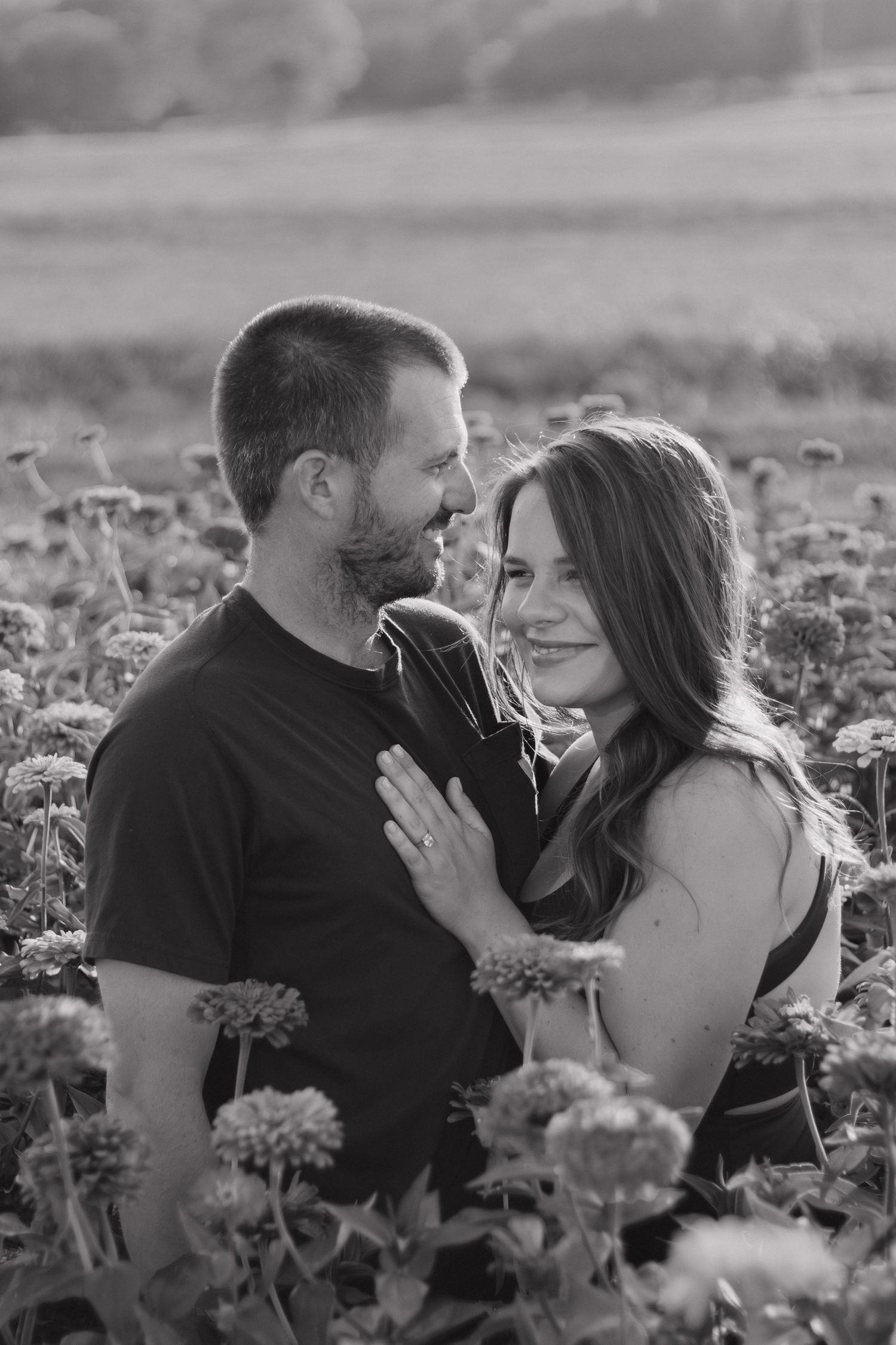 Black and white photo of a couple embracing in a flower field, sharing a tender moment while gazing at each other.