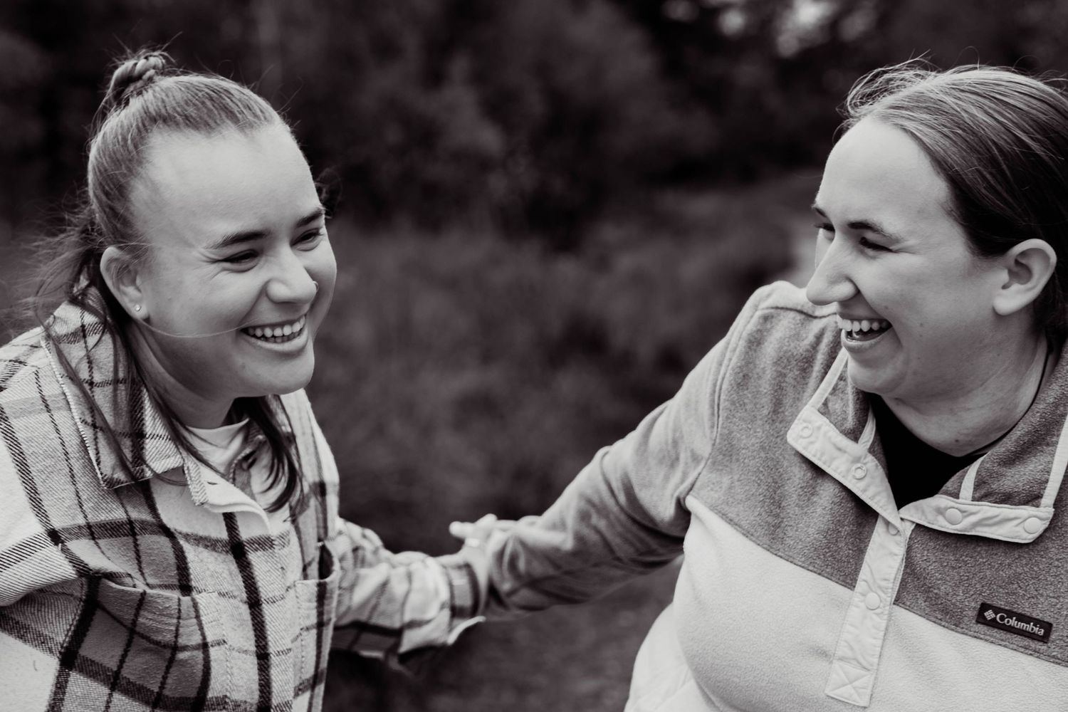Two smiling women laughing together outdoors in a black and white couples portrait photo.