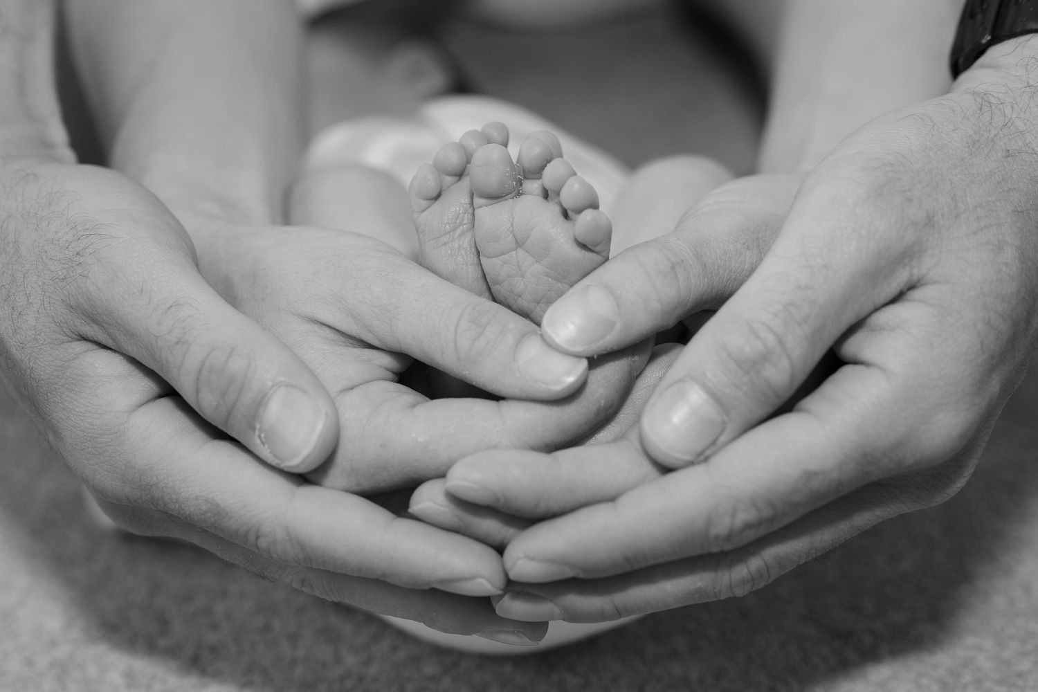 Black and white detail of newborn baby feet and parents hands