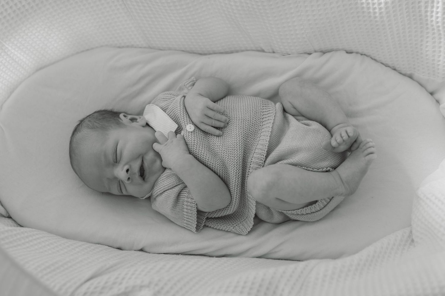 Black and white photo of a peaceful newborn baby sleeping in a soft white nest.