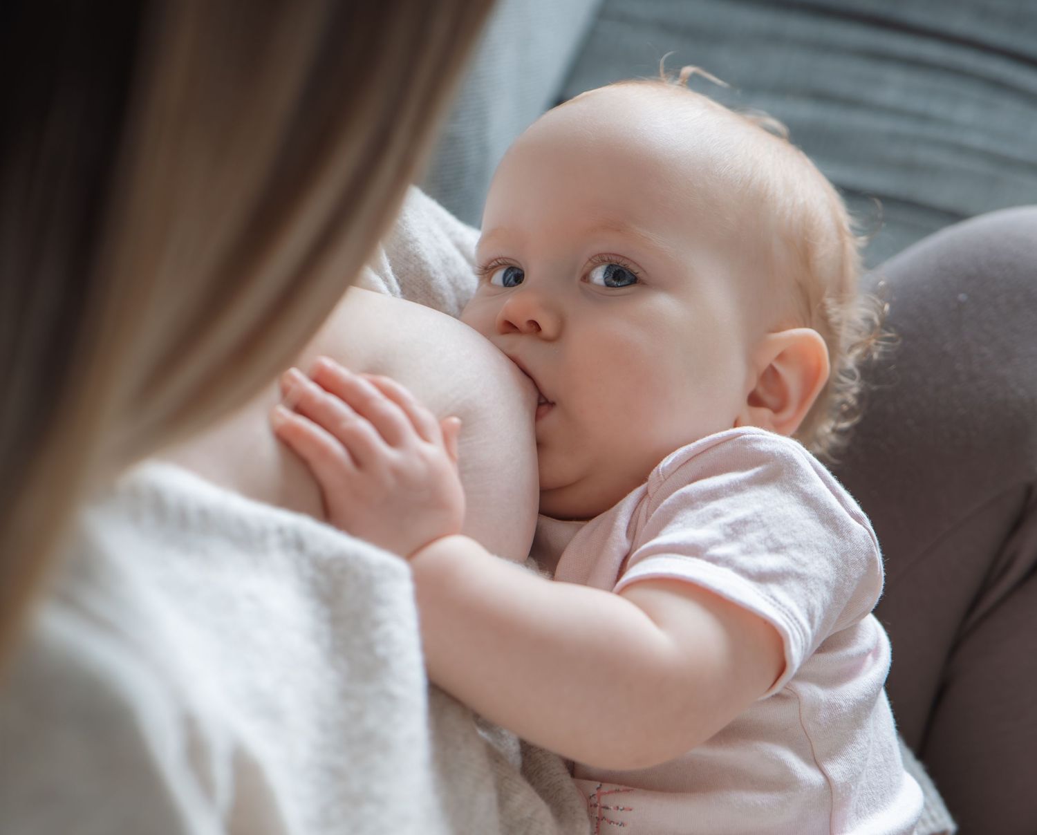 Close-up of a baby with blue eyes breastfeeding while looking up at their mother.