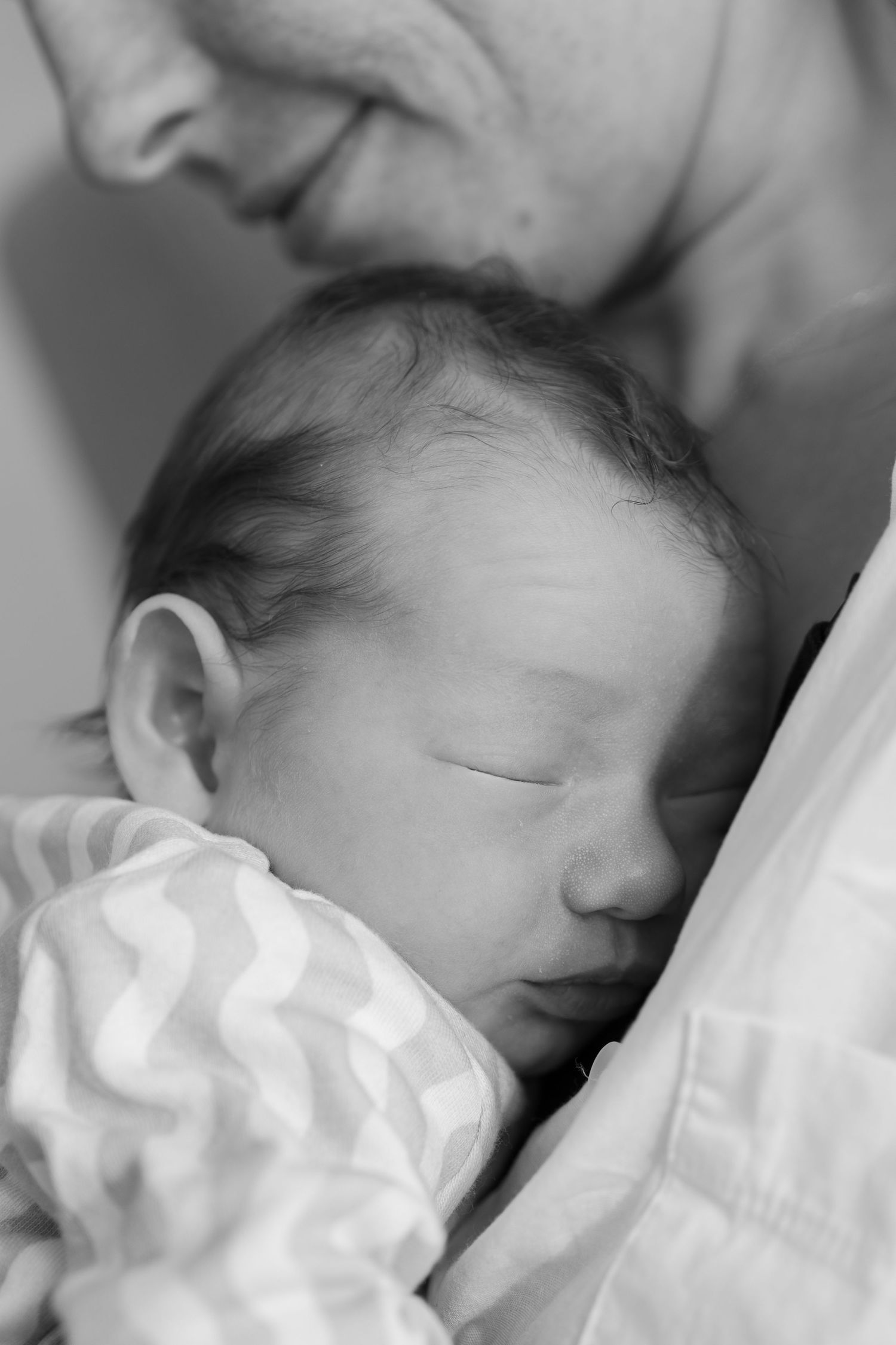 Black and white close-up of sleeping newborn baby nestled against parent's chest.
