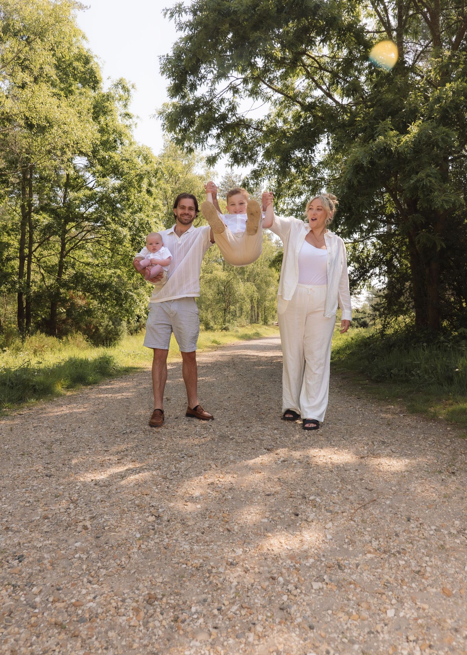 Young family laughing and swinging a child in the woods