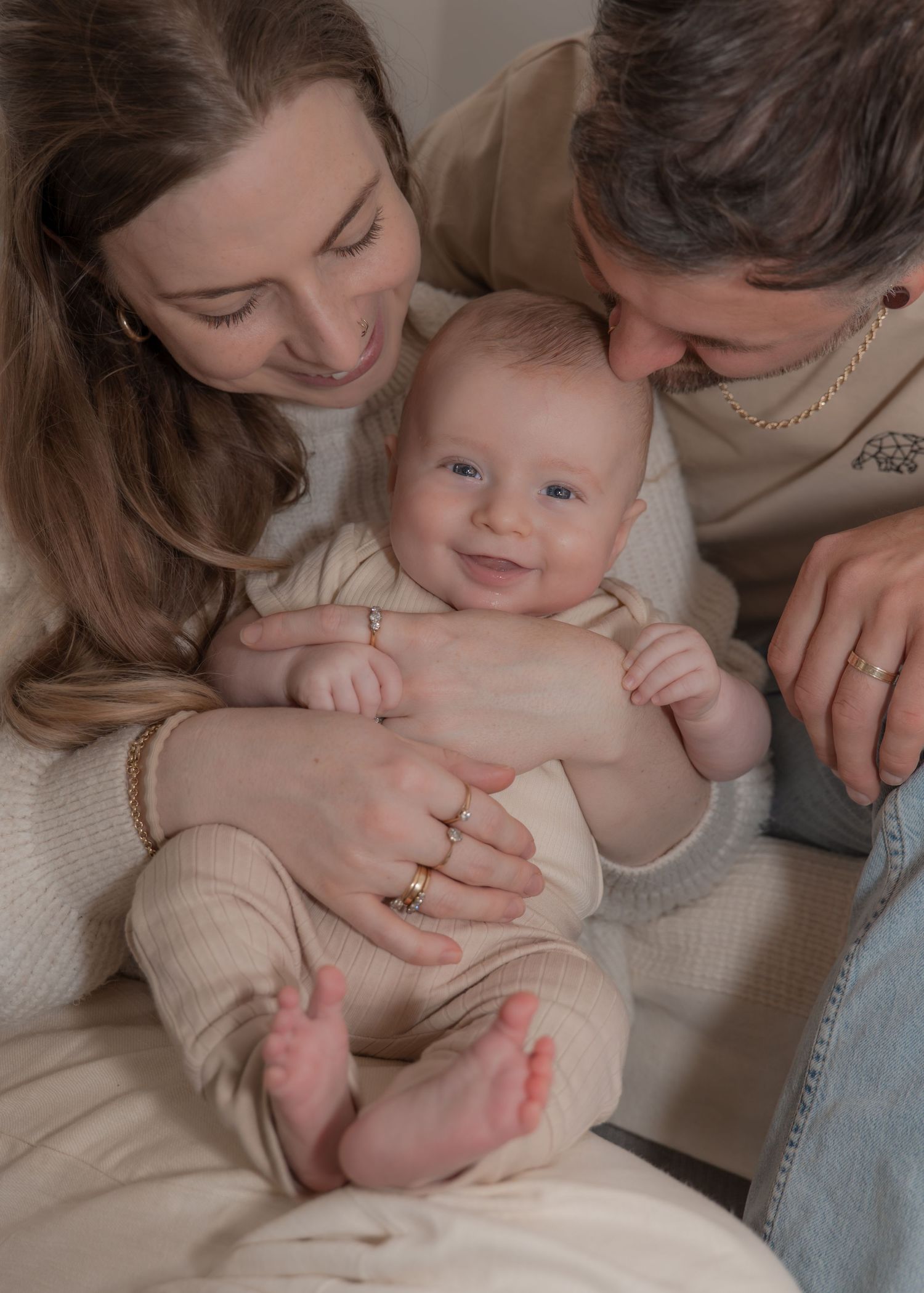 Two smiling parents lovingly hold their happy baby, who gazes at the camera in a warm family portrait.